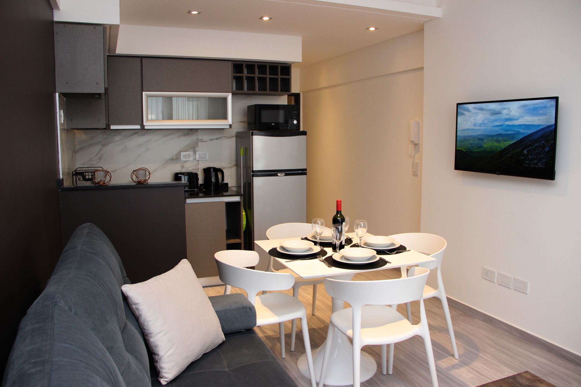 Modern studio apartment with sofa, dining table set, kitchenette, and wall-mounted TV
