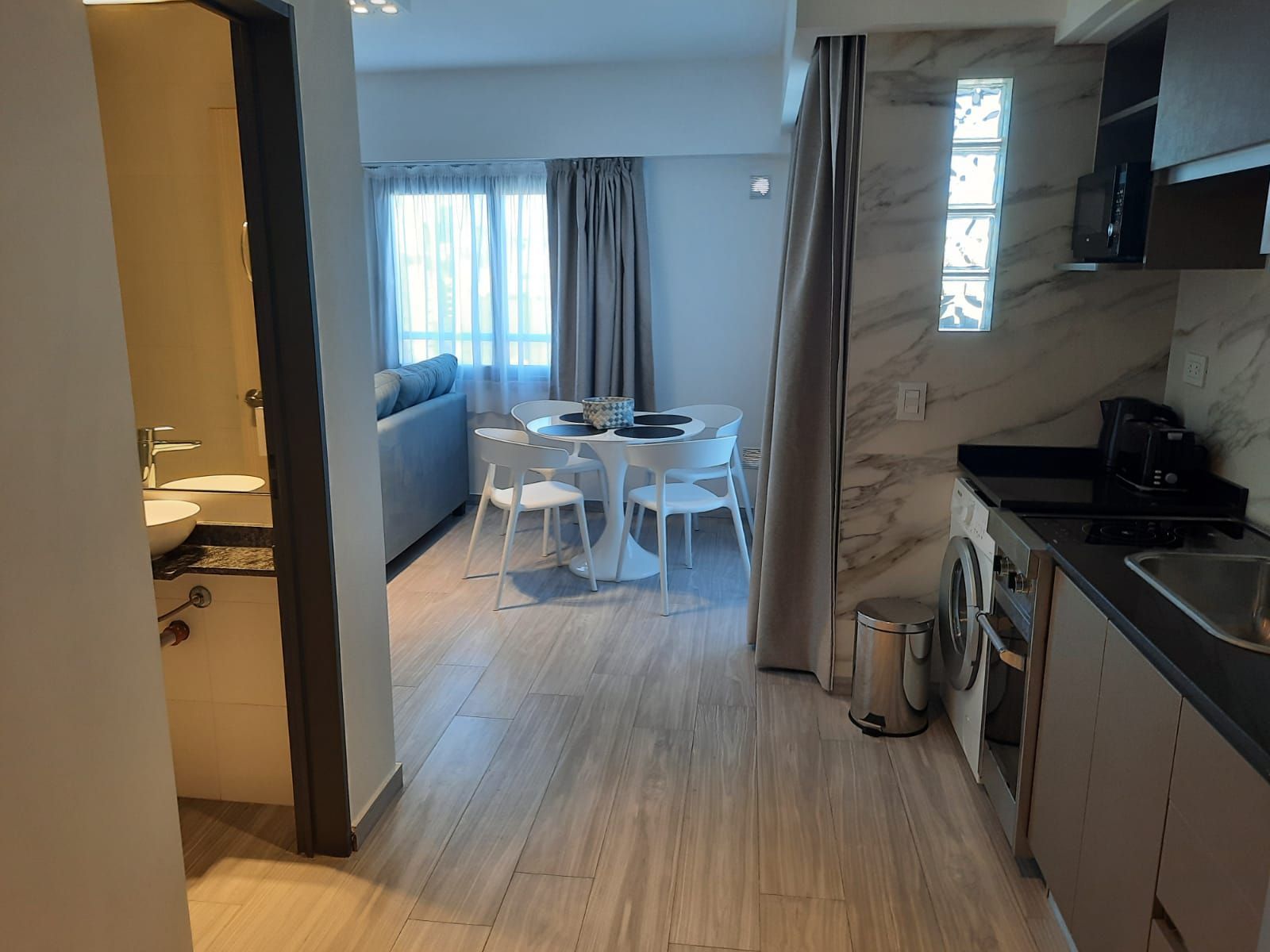Modern apartment kitchen and dining area with white table, chairs, and large window in the background