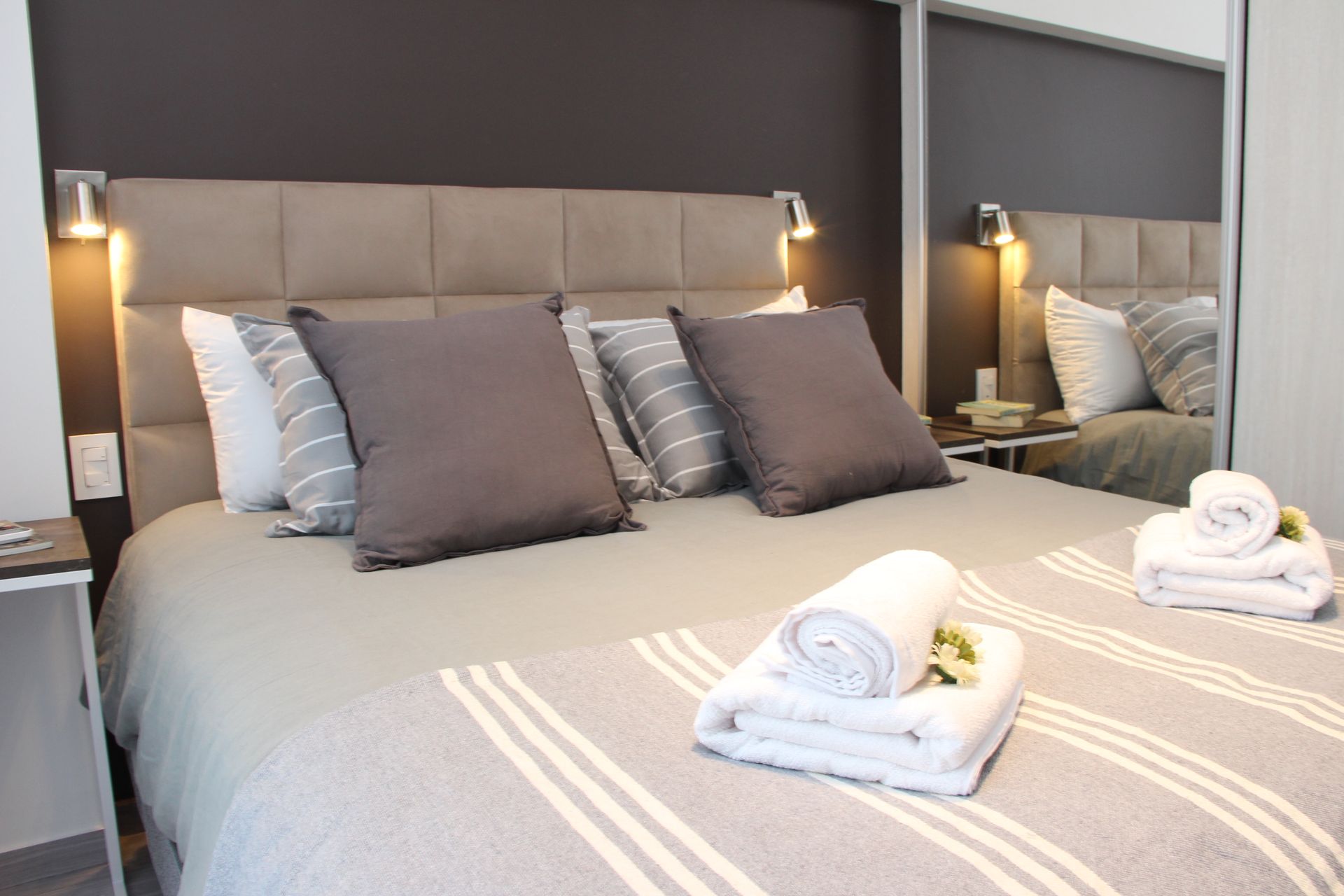 Modern bedroom with a neatly made bed, gray bedding, and rolled towels on top
