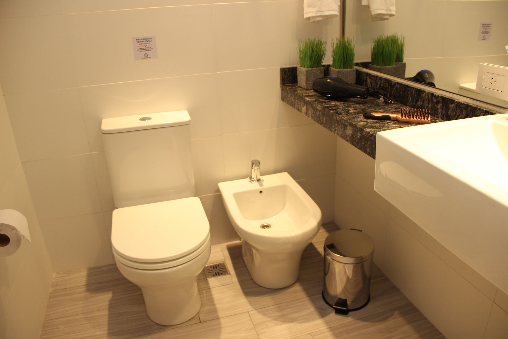 Modern bathroom with toilet, bidet, sink, and dark countertop with potted plants