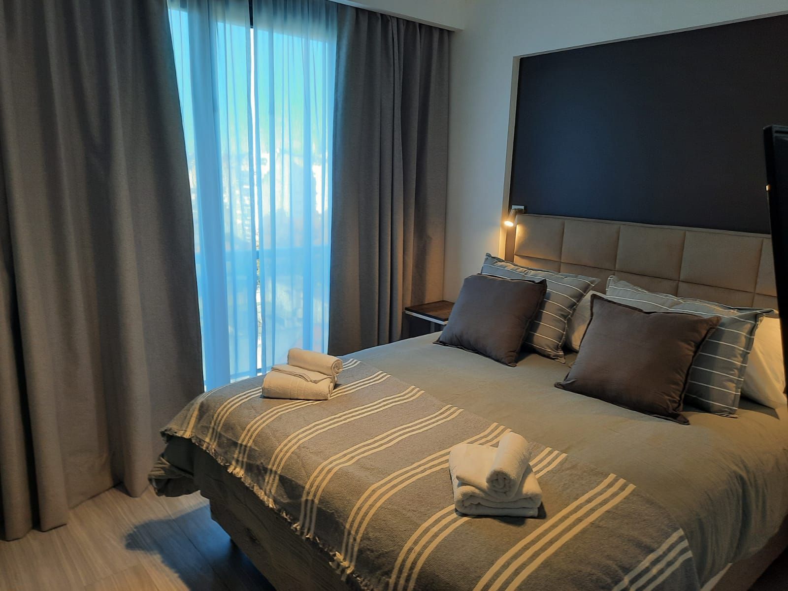 Cozy bedroom with a neatly made bed, gray curtains, and soft natural light from a window