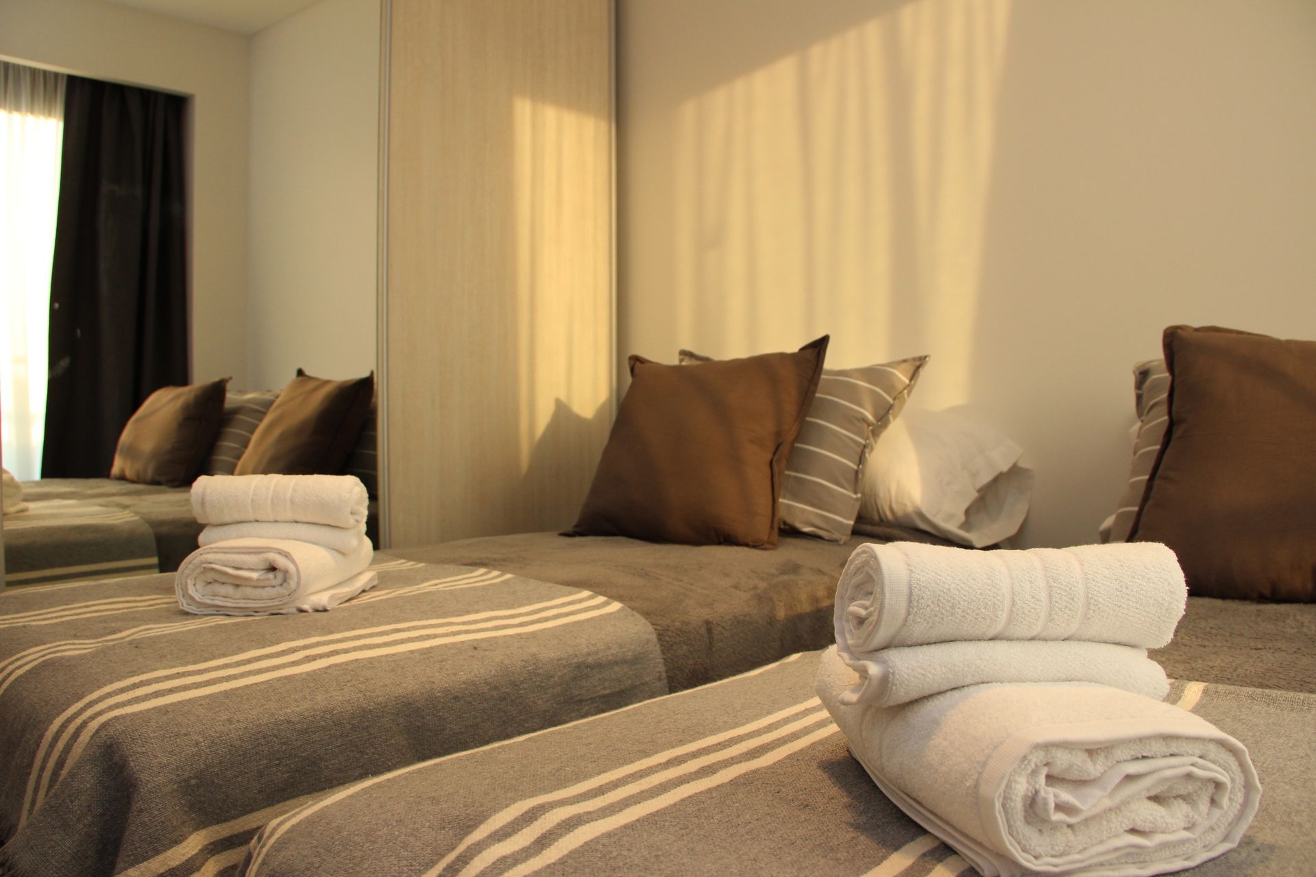 Neatly made twin beds in a warm hotel room with beige walls and folded white towels