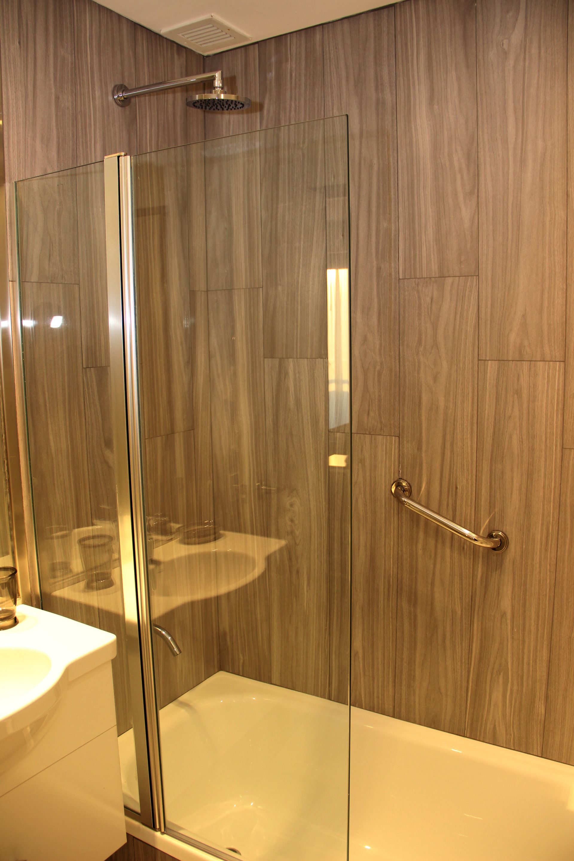 Bathroom with a glass shower enclosure, wood-pattern walls, and a bathtub with chrome fixtures.