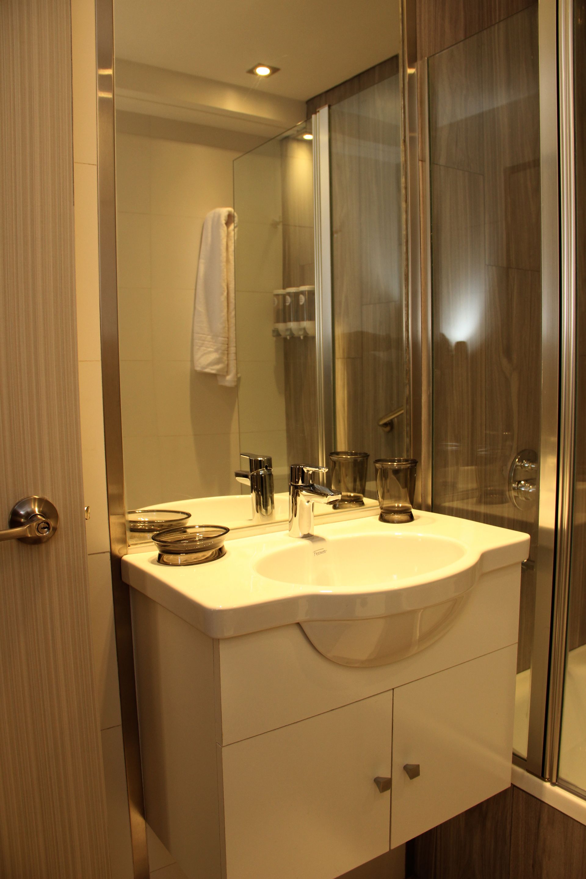 Small bathroom vanity with sink, mirror, towels, and glass shower enclosure