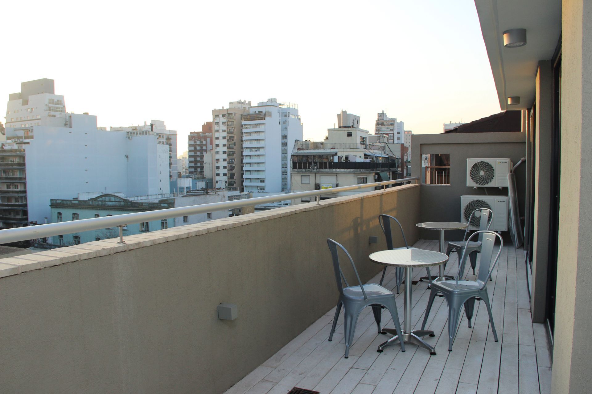 Balcony with table and chairs overlooking city buildings at sunset