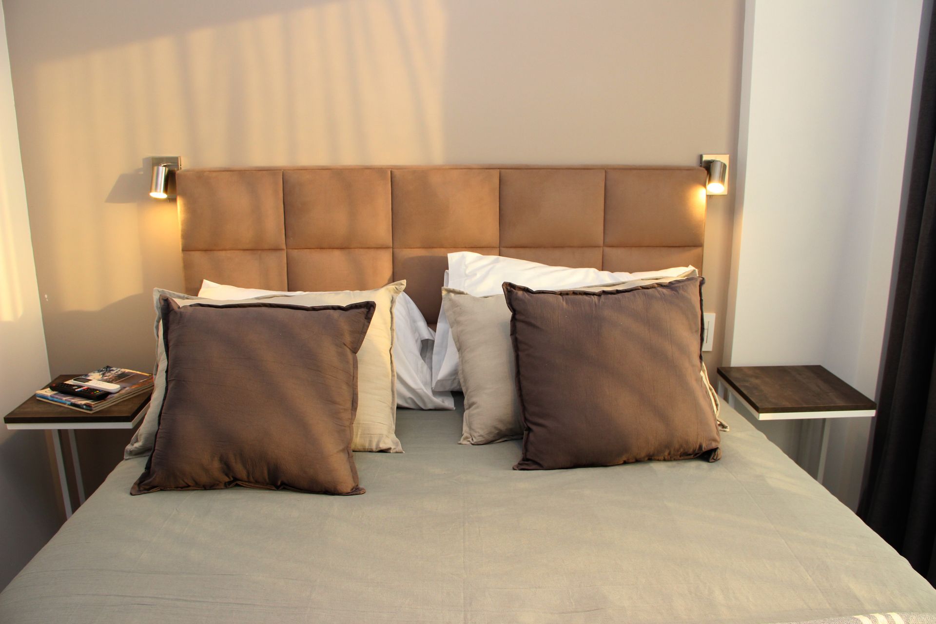 Neatly made bed with beige headboard, white pillows, and bedside lamps in a softly lit bedroom