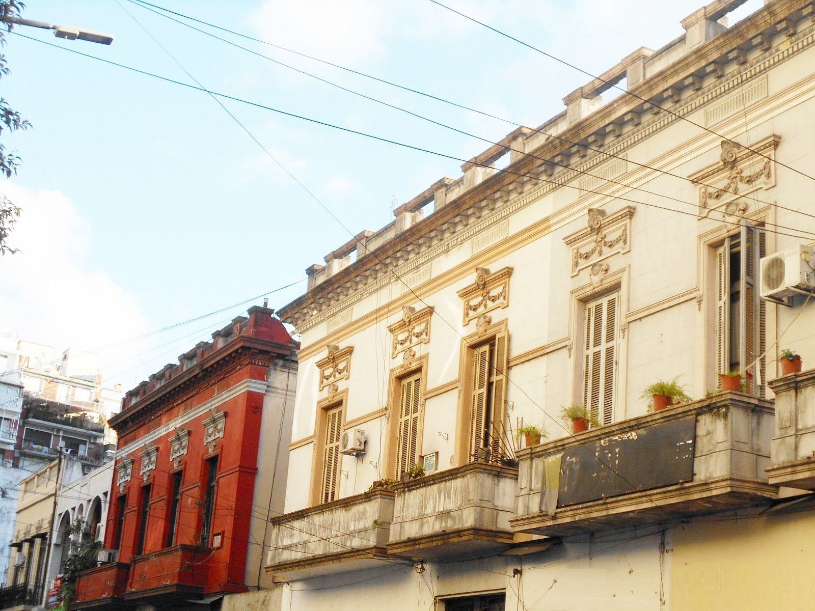 Historic street with colorful old balconies and facades, including a red building beside a cream-colored one