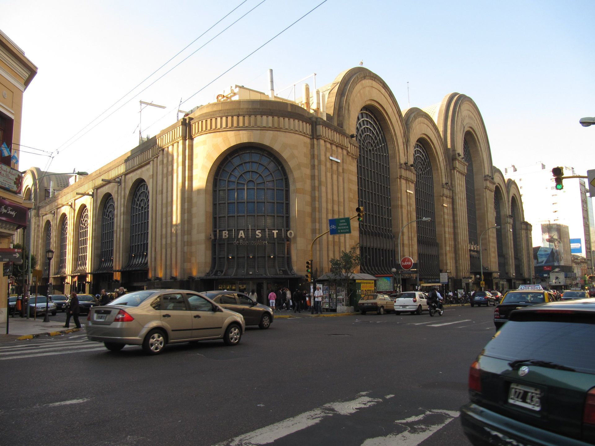 Grand stone train station with arched windows on a busy city street, cars passing in front