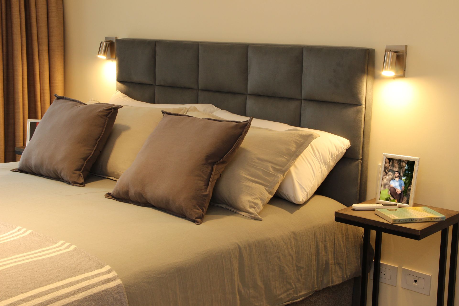 Cozy bedroom with a dark tufted headboard, beige bedding, and bedside lamps with warm light.