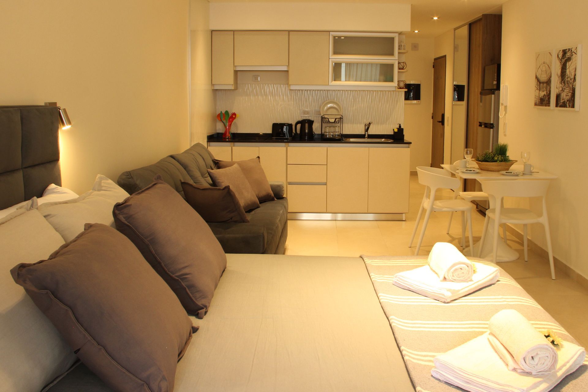 Cozy studio apartment with a bed, kitchenette, and small dining area in warm beige tones