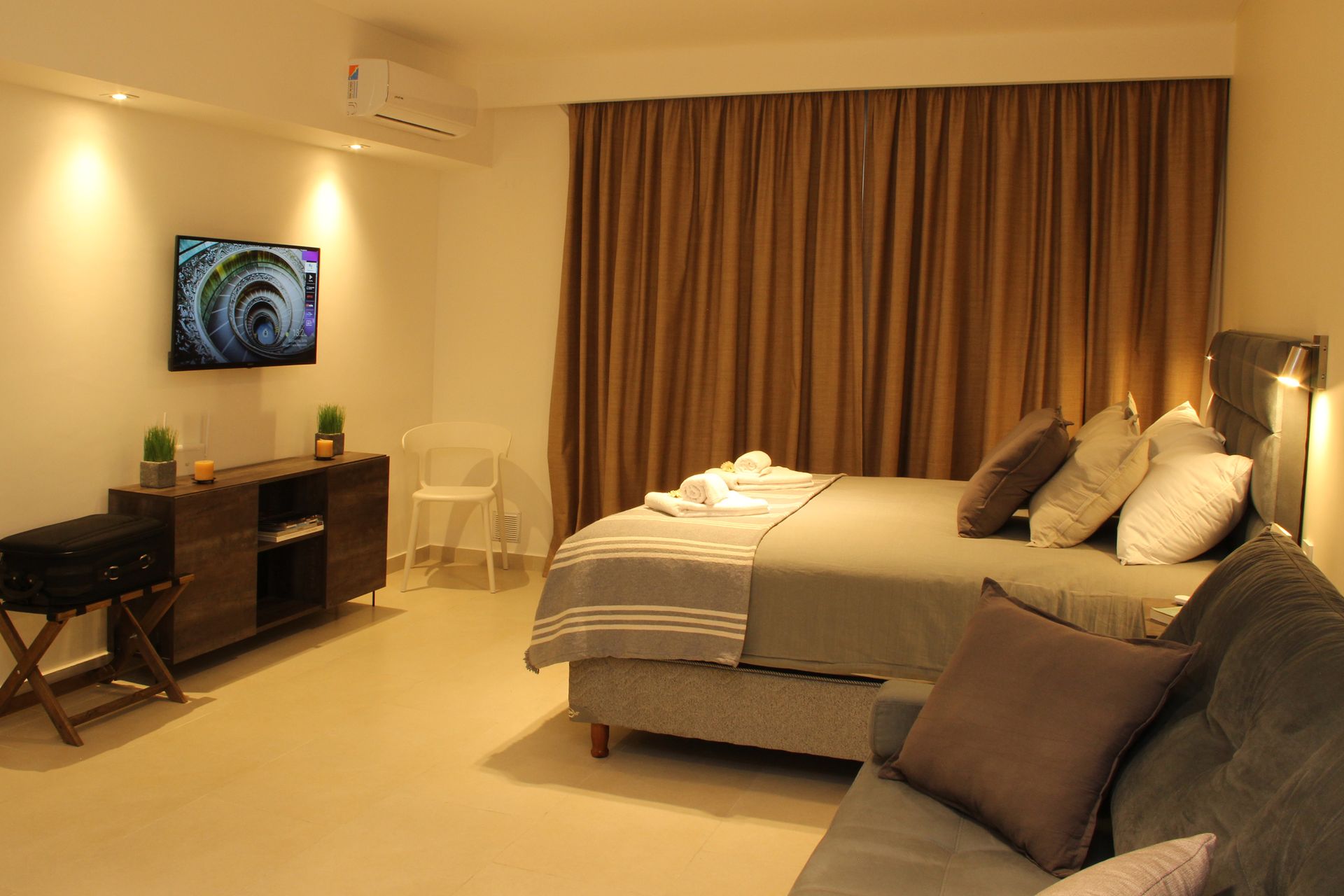 Modern hotel room with a bed, TV, desk, chair, and beige curtains