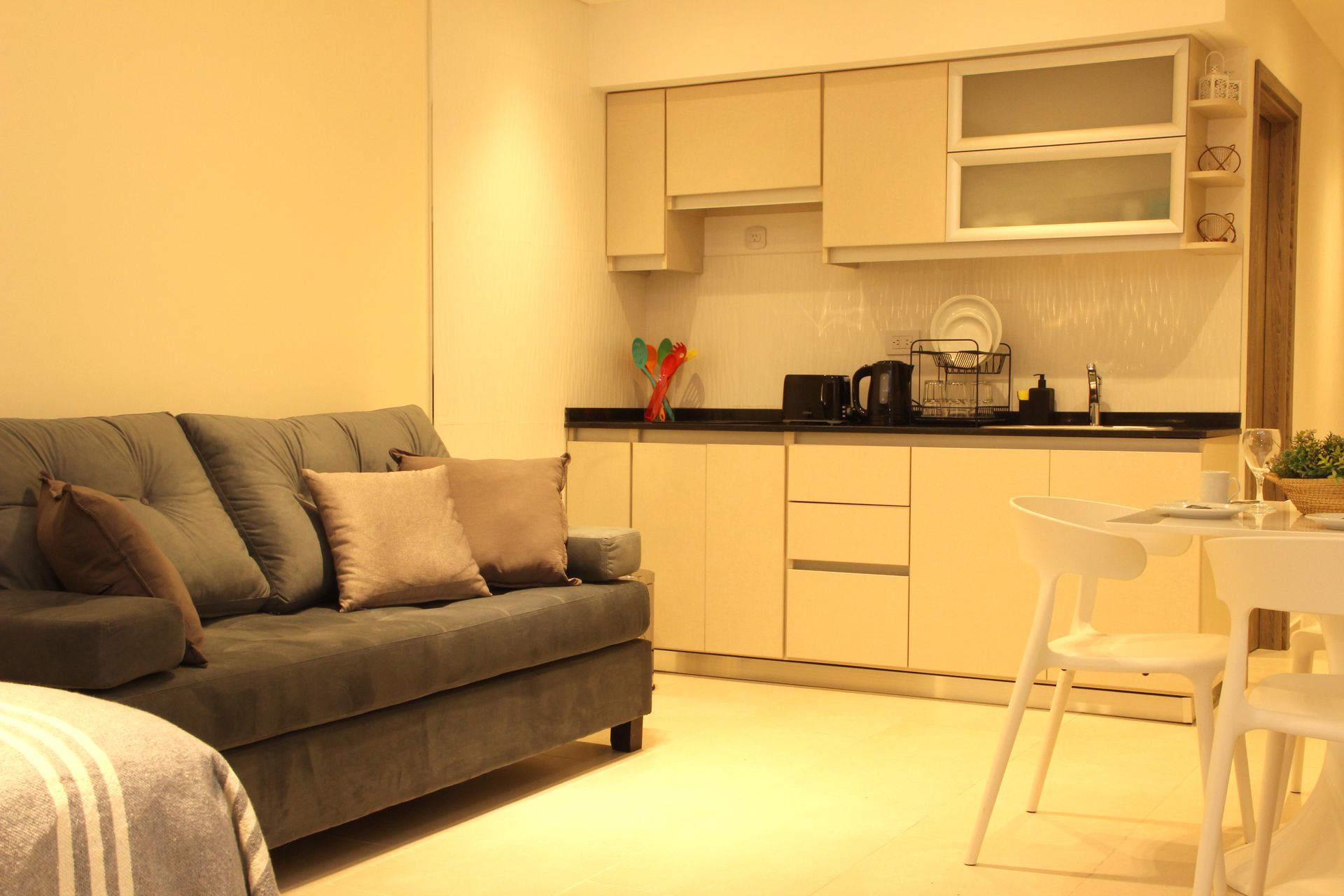 Cozy living room with gray sofa and small kitchen nook in warm yellow lighting