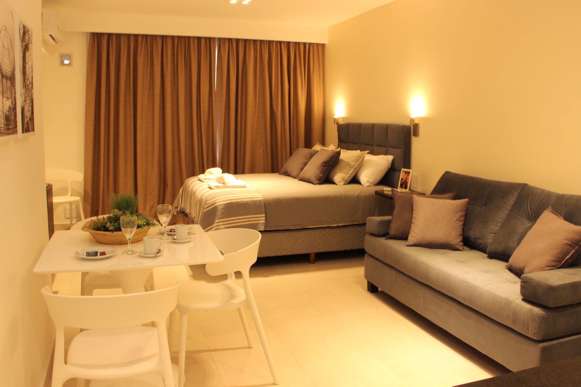 Modern studio room with a bed, gray sofa, dining table, and warm lighting