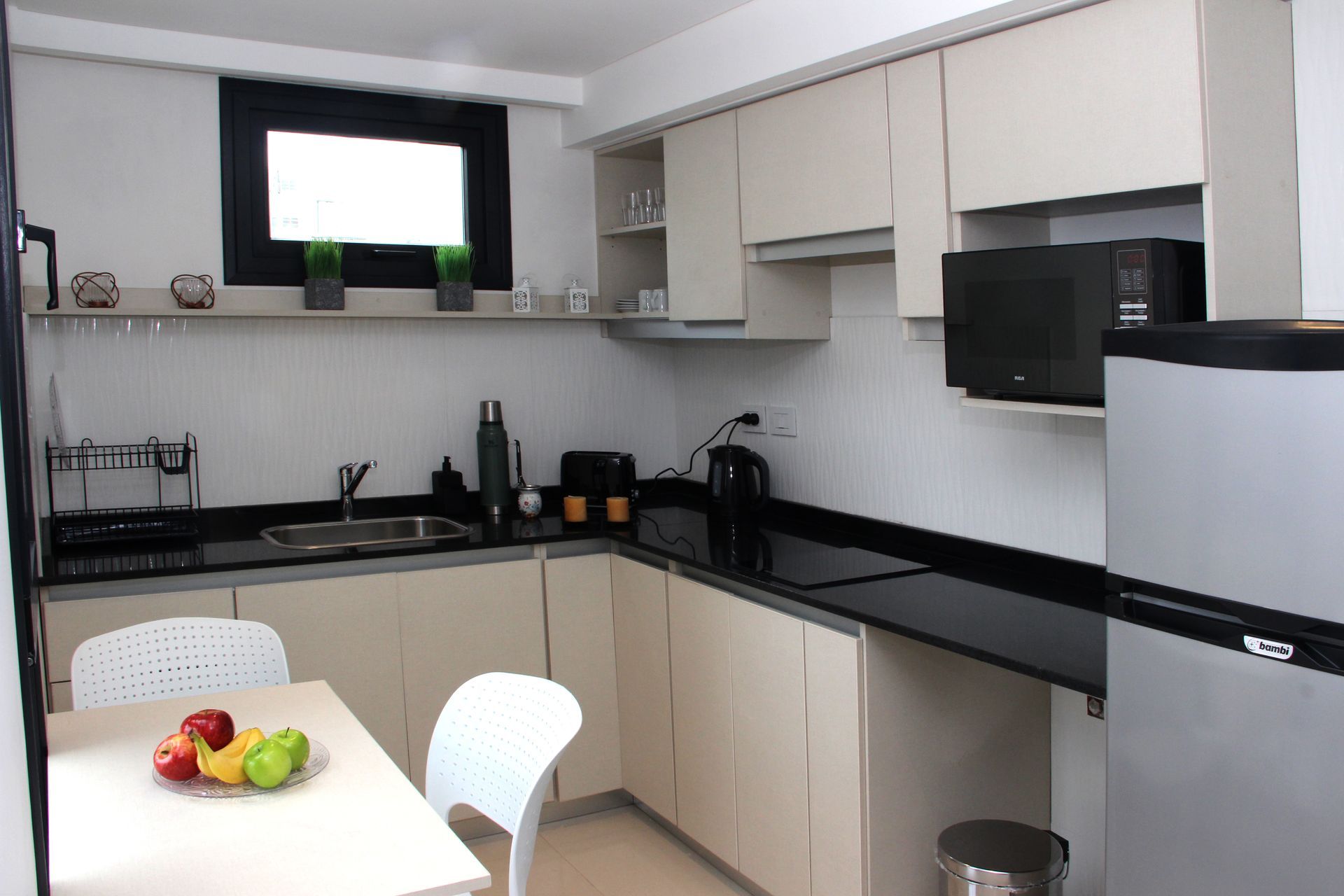 Modern kitchen with beige cabinets, black countertops, white dining table, and fruit bowl