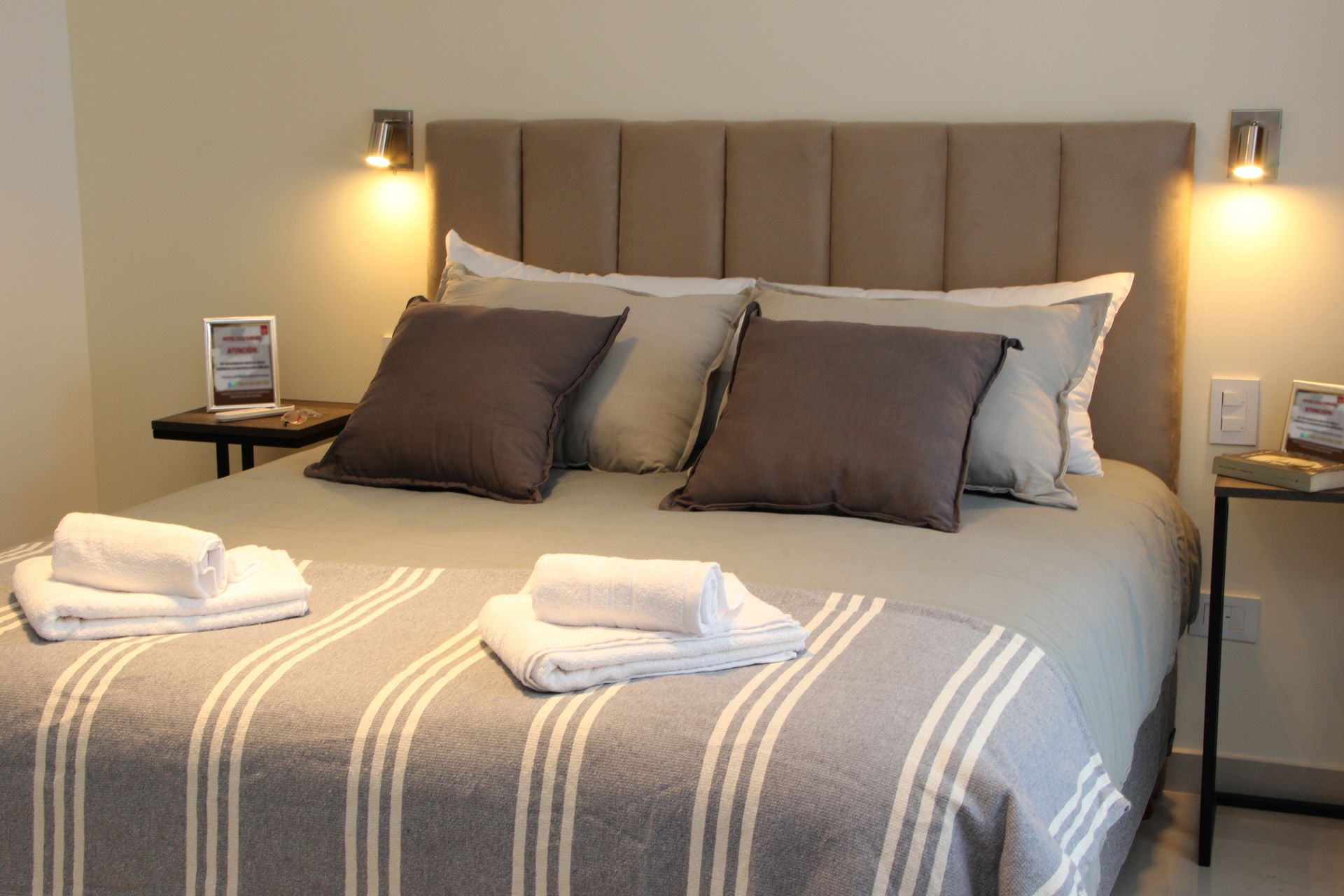 Neatly made bed with gray bedding, striped throw, and towels in a softly lit bedroom.