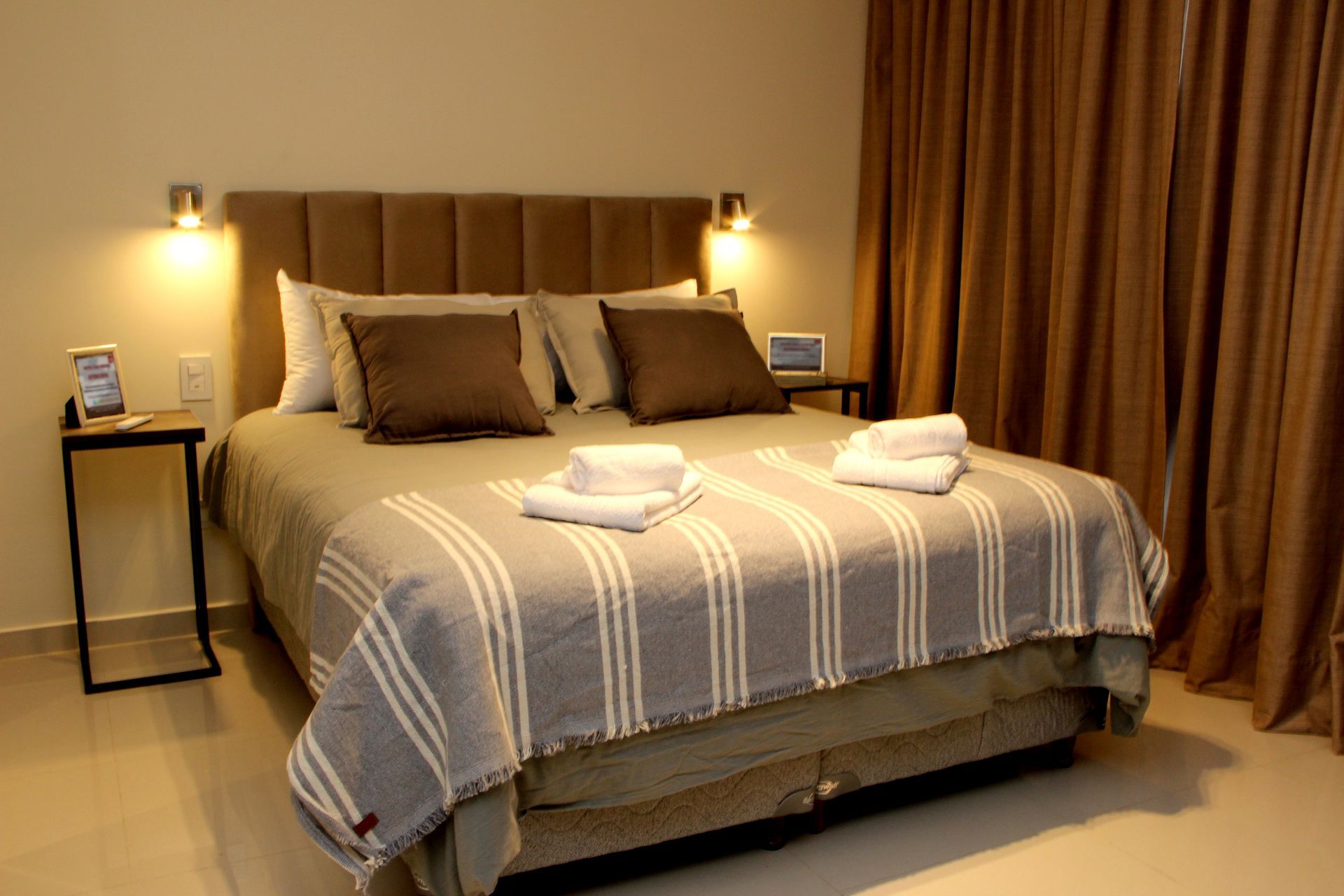 Cozy bedroom with a neatly made bed, bedside lamps, and folded towels at the foot.