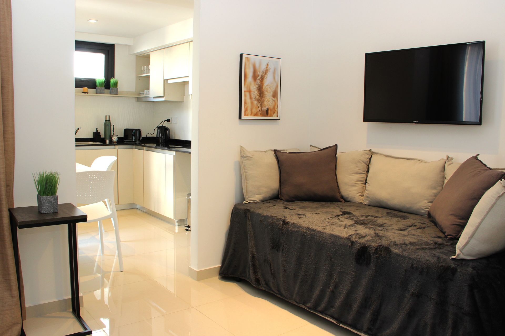Modern living room with black sofa, wall-mounted TV, and open kitchen in the background