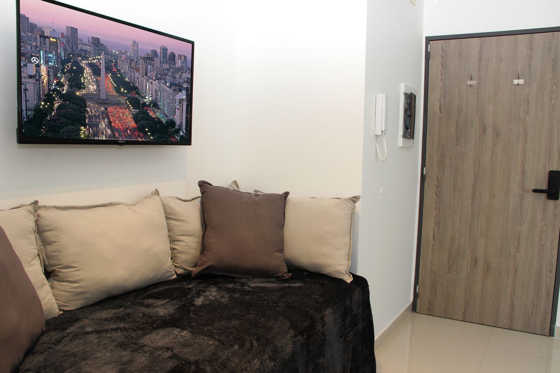 Living room with beige sofa, dark throw, cityscape wall art, and a wooden door on the right.