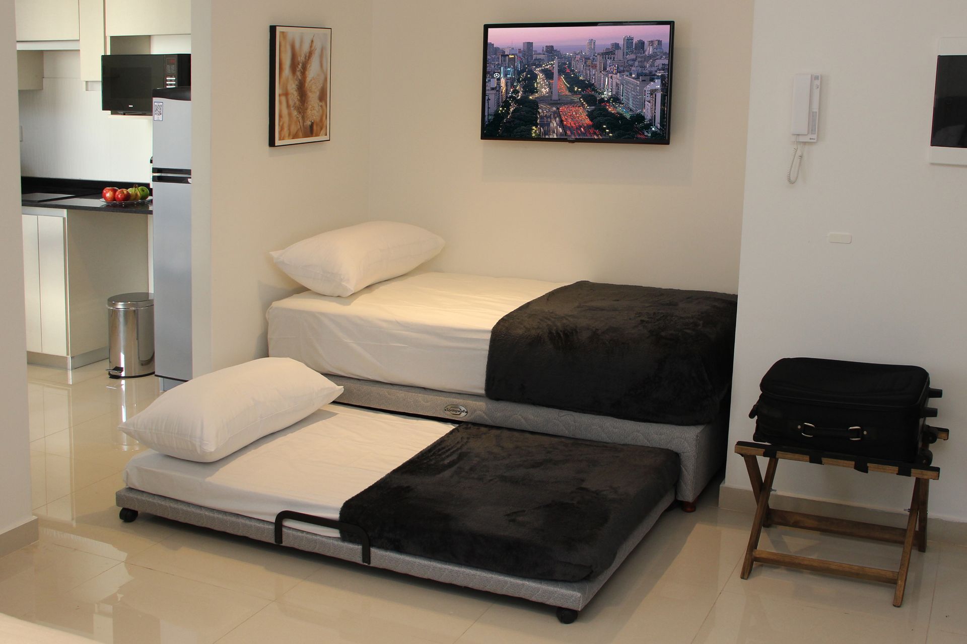Small studio with two low beds, wall-mounted TV, and kitchenette in the background.