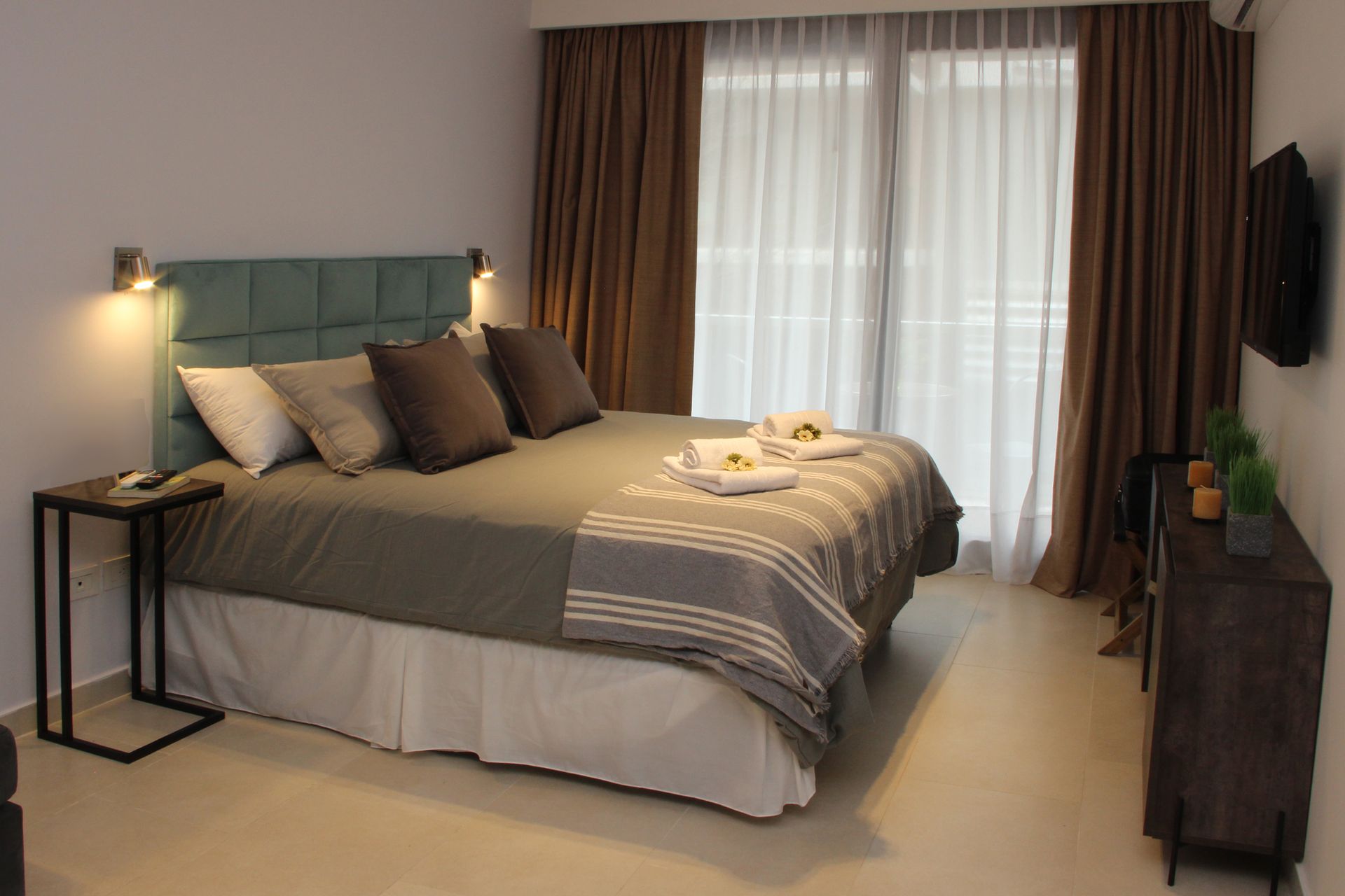 Modern bedroom with a gray bed, bedside lamp, dark curtains, and a dresser by a window