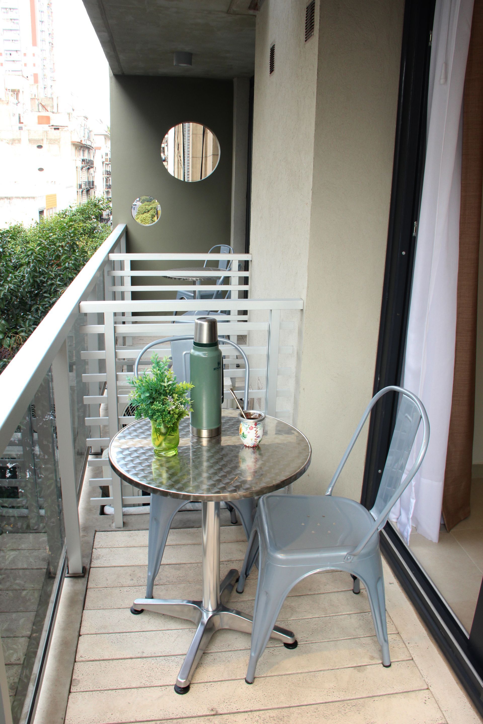 Small balcony with a metal table and chair, potted plants, and a sliding glass door.