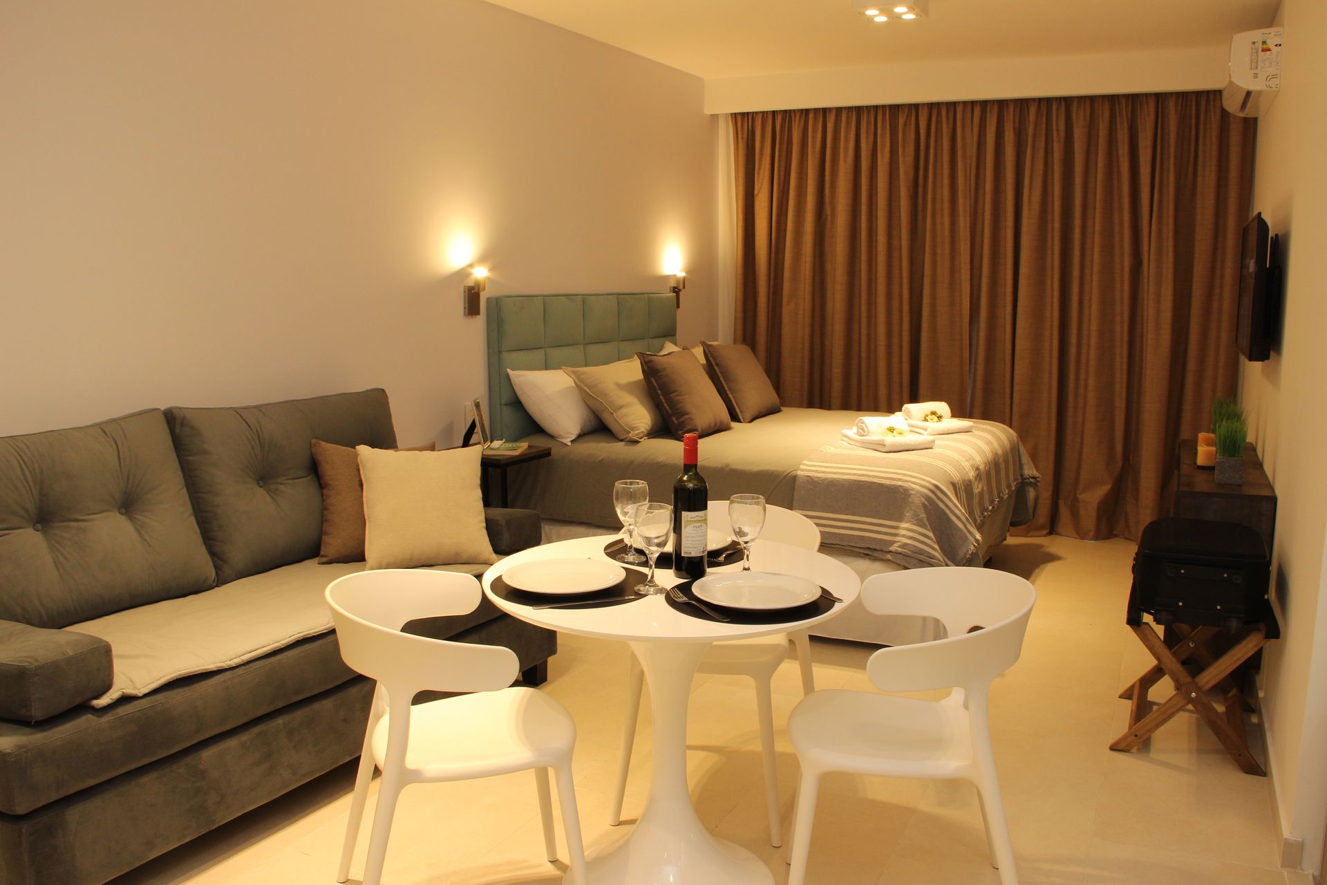 Cozy bedroom with sofa, round table set for dinner, and a bed beside closed curtains