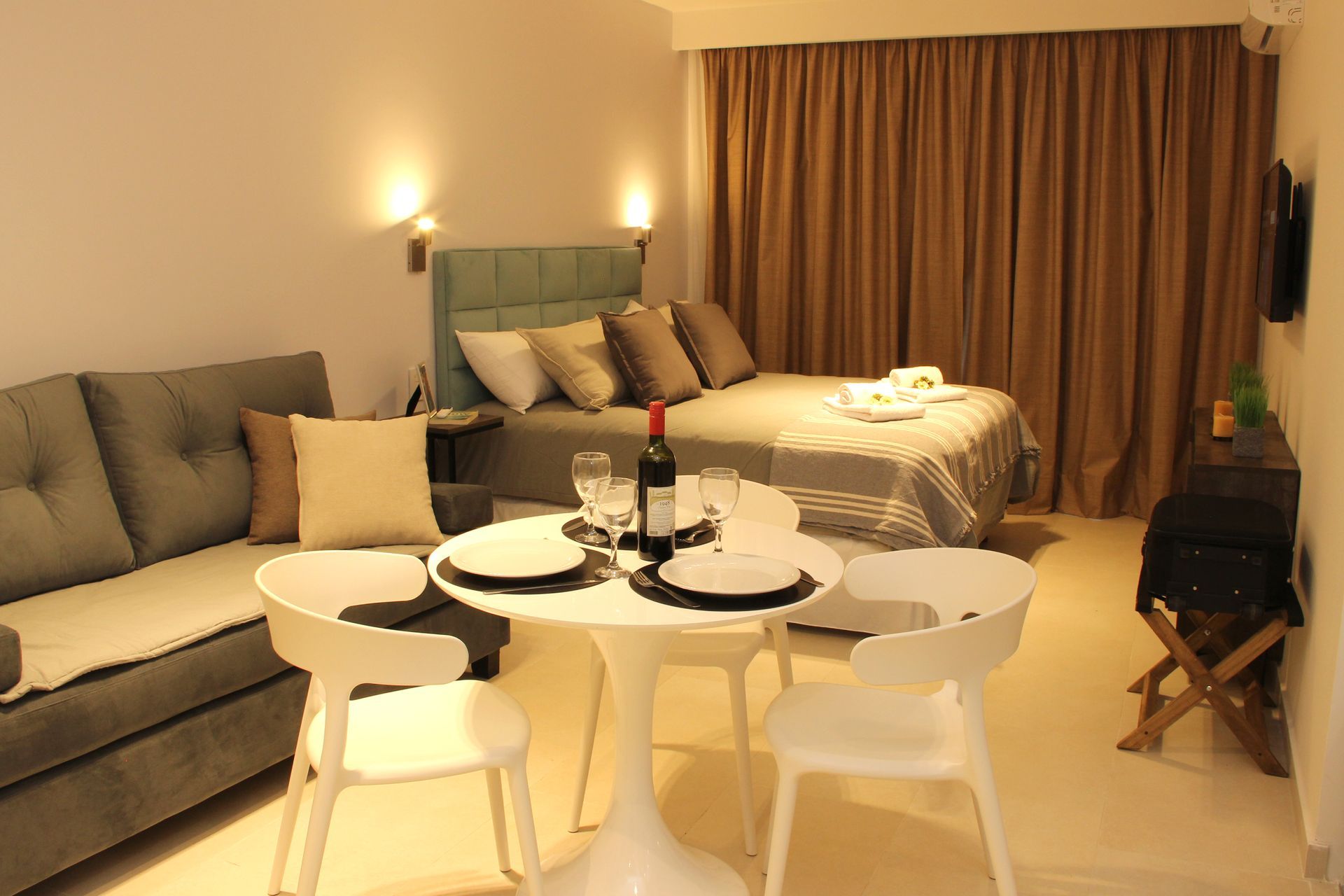 Cozy hotel room with bed, sofa, dining table, and warm lighting