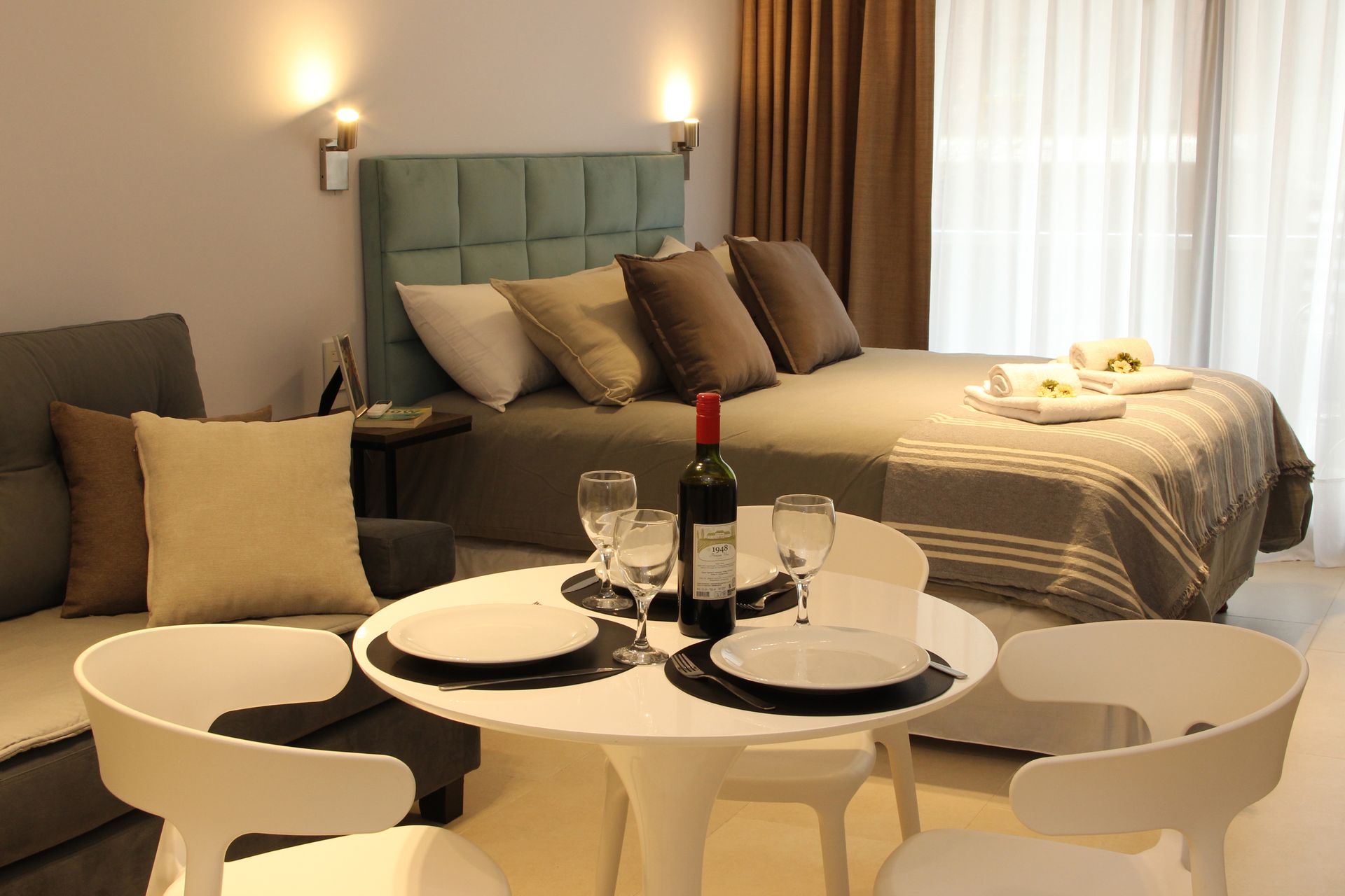 Modern hotel room with a bed, round dining table, and wine bottle on the table