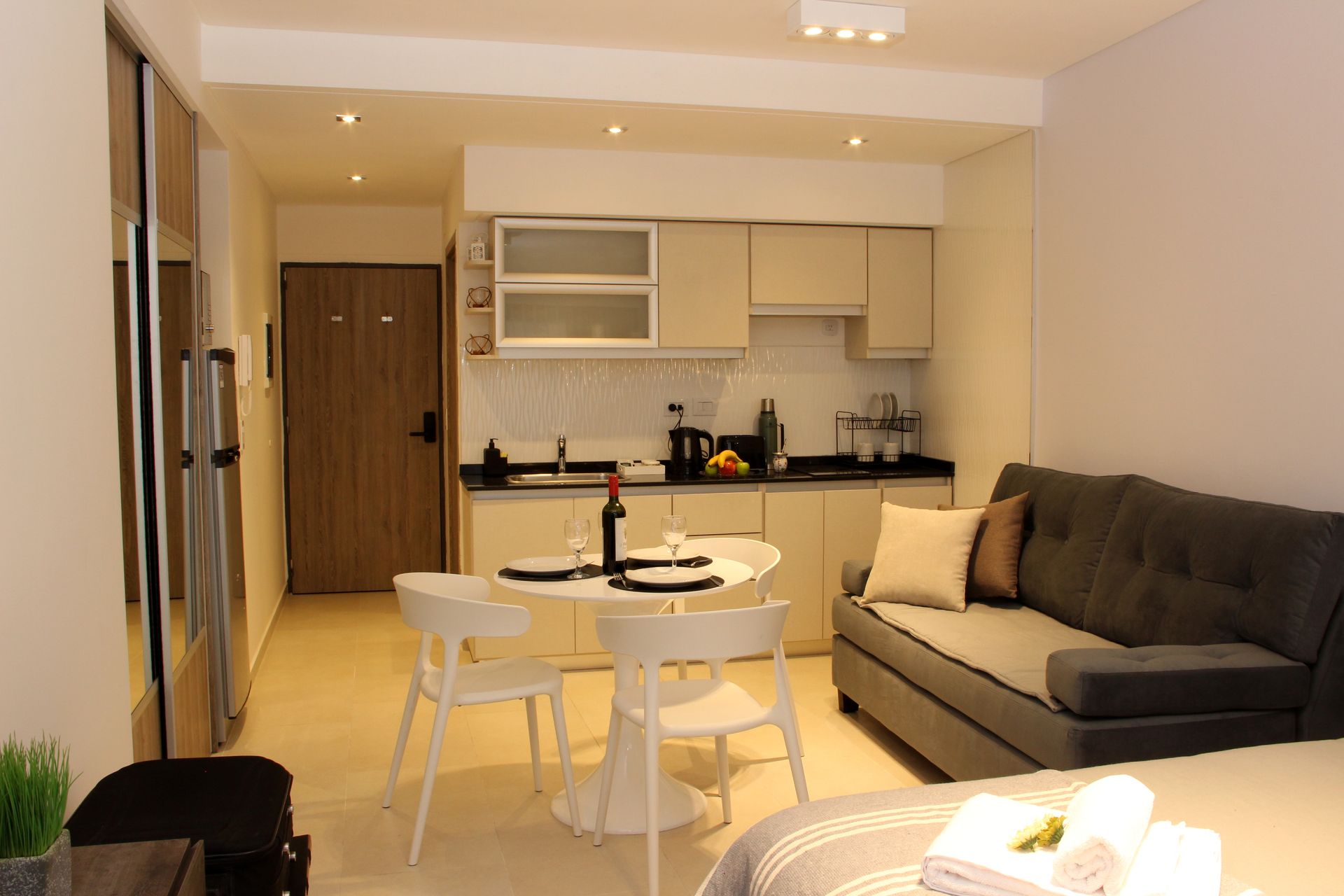 Modern open-plan apartment with kitchen, dining table, and gray sofa in warm lighting