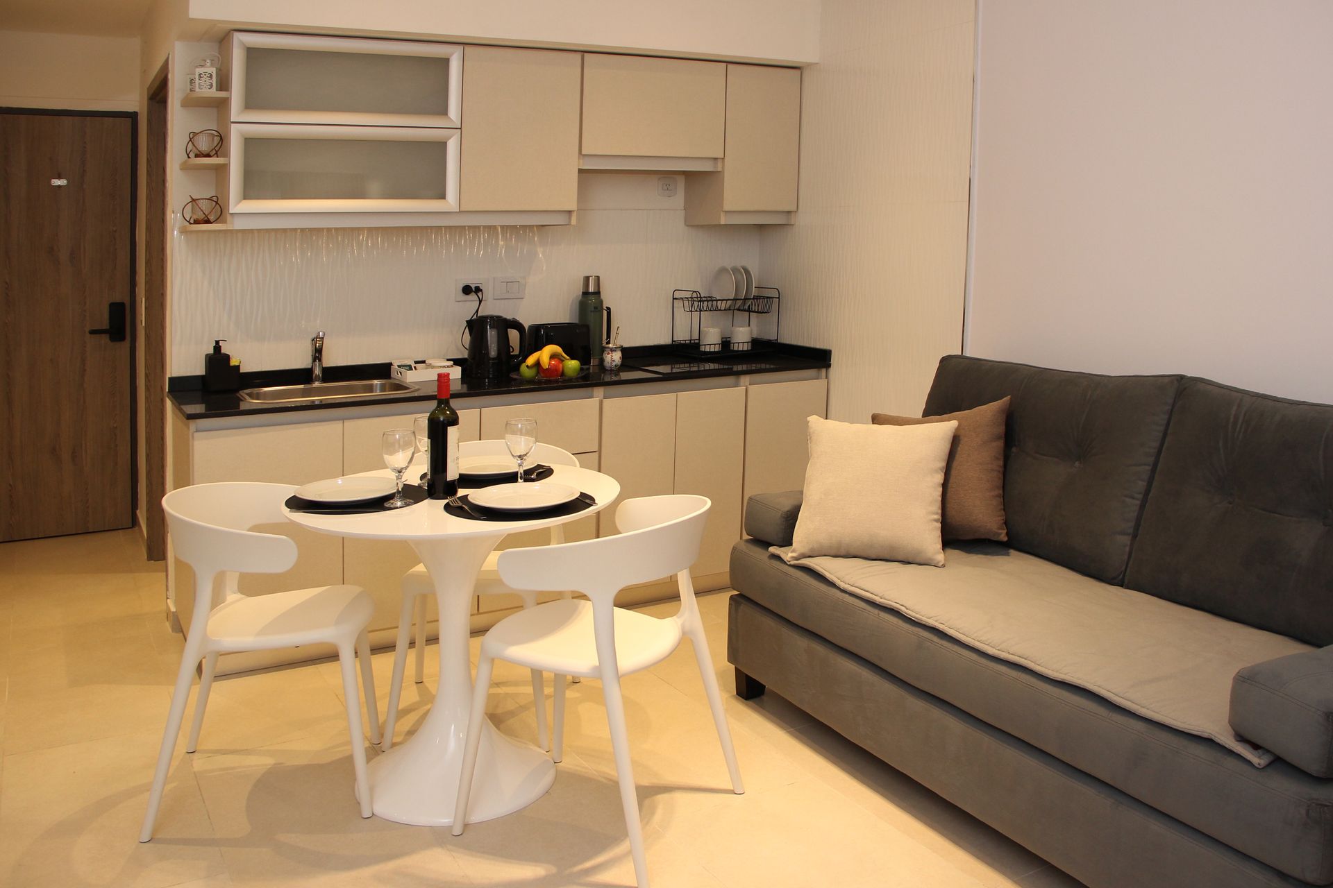 Modern open-plan kitchen and living room with white dining set, gray sofa, and beige cabinets