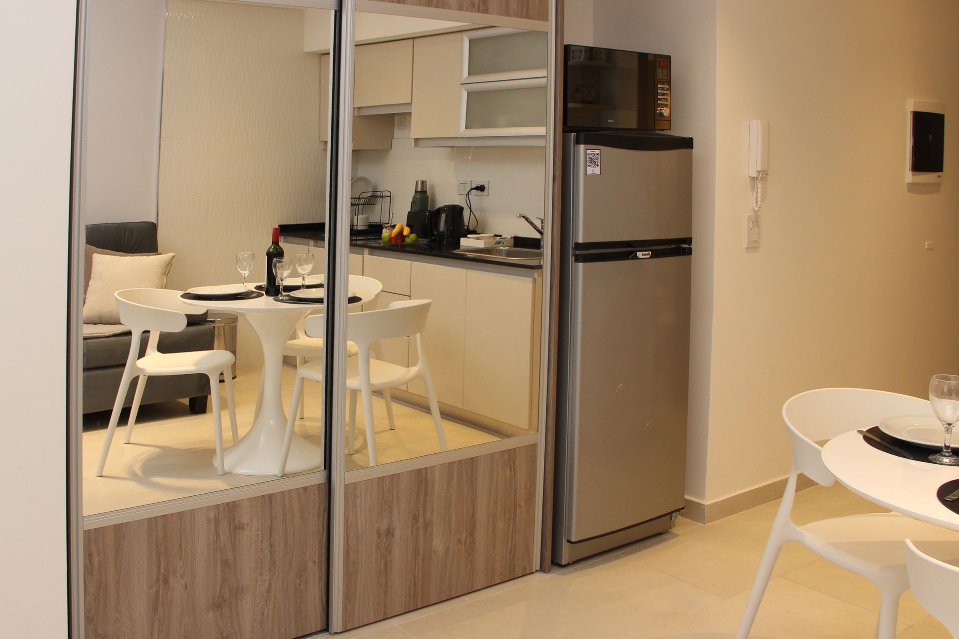 Modern kitchenette and dining area with mirrored cabinets, wood accents, and a stainless refrigerator