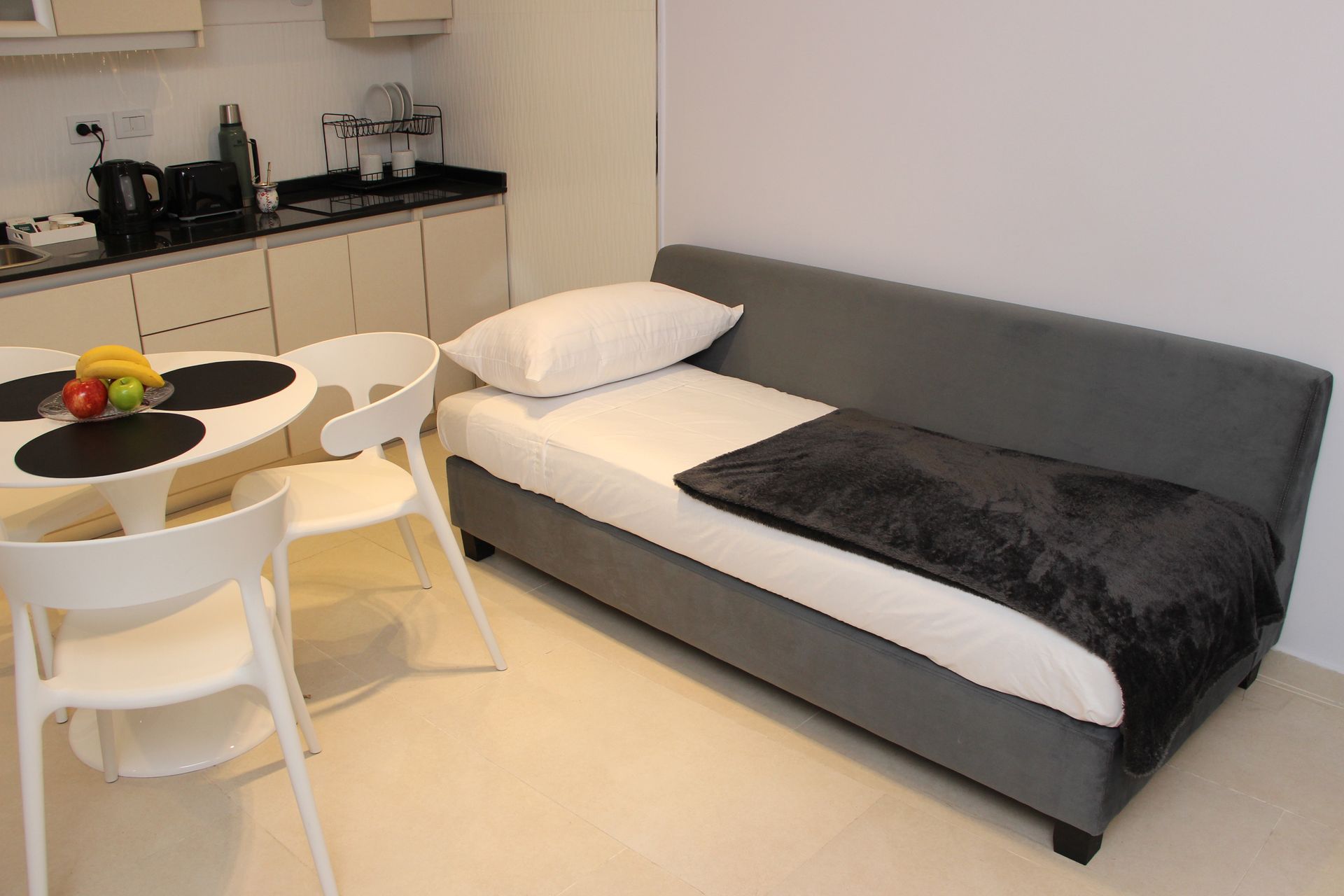 Modern studio bedroom with gray sofa bed, small dining table, and kitchenette