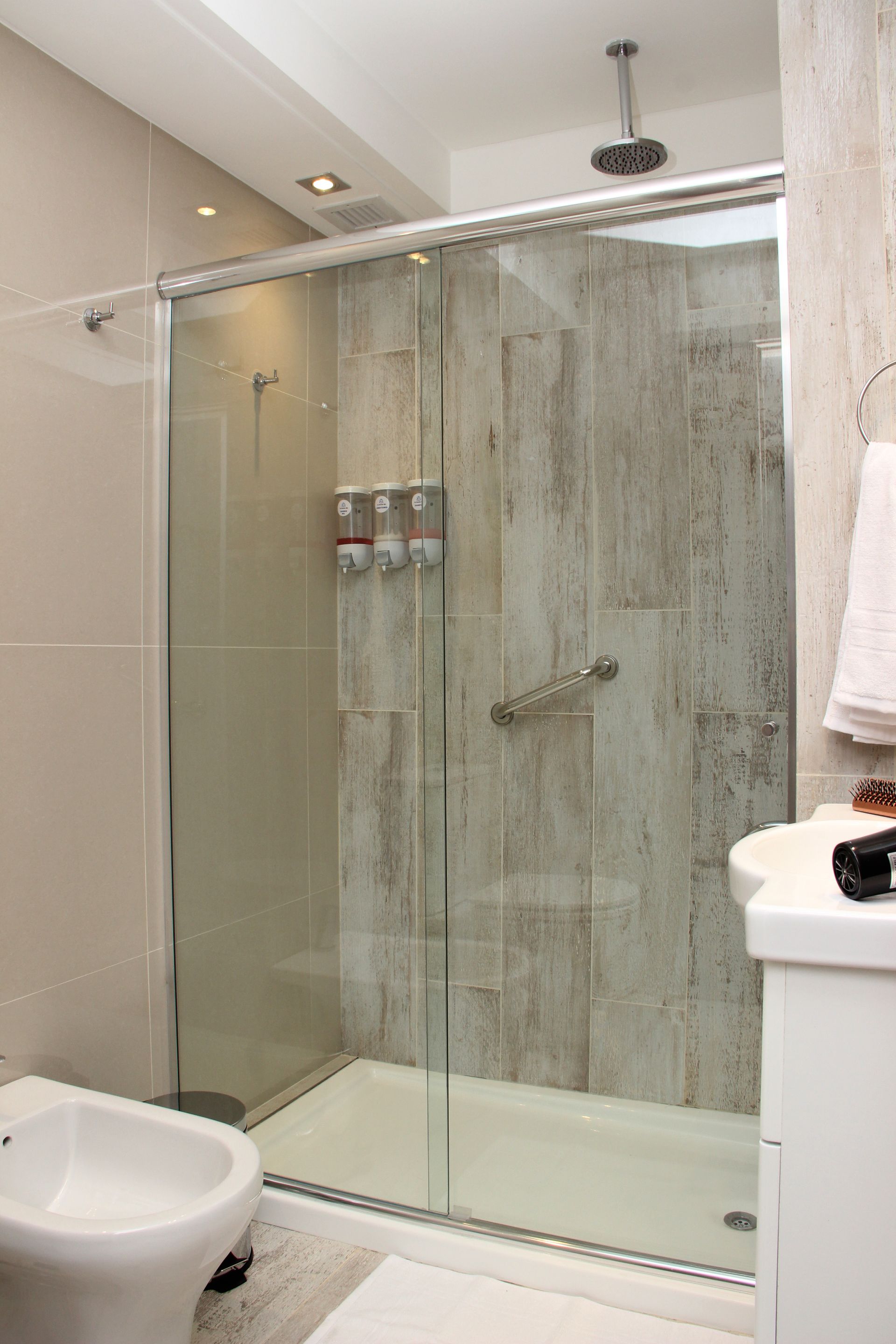 Modern bathroom with glass walk-in shower, gray tile walls, and a toilet in the foreground