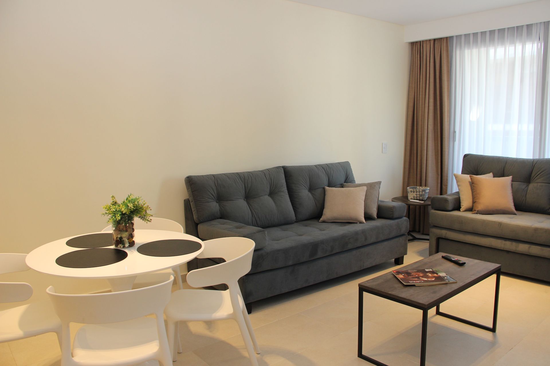 Modern living room with gray sofa, white dining table, coffee table, and large window curtains
