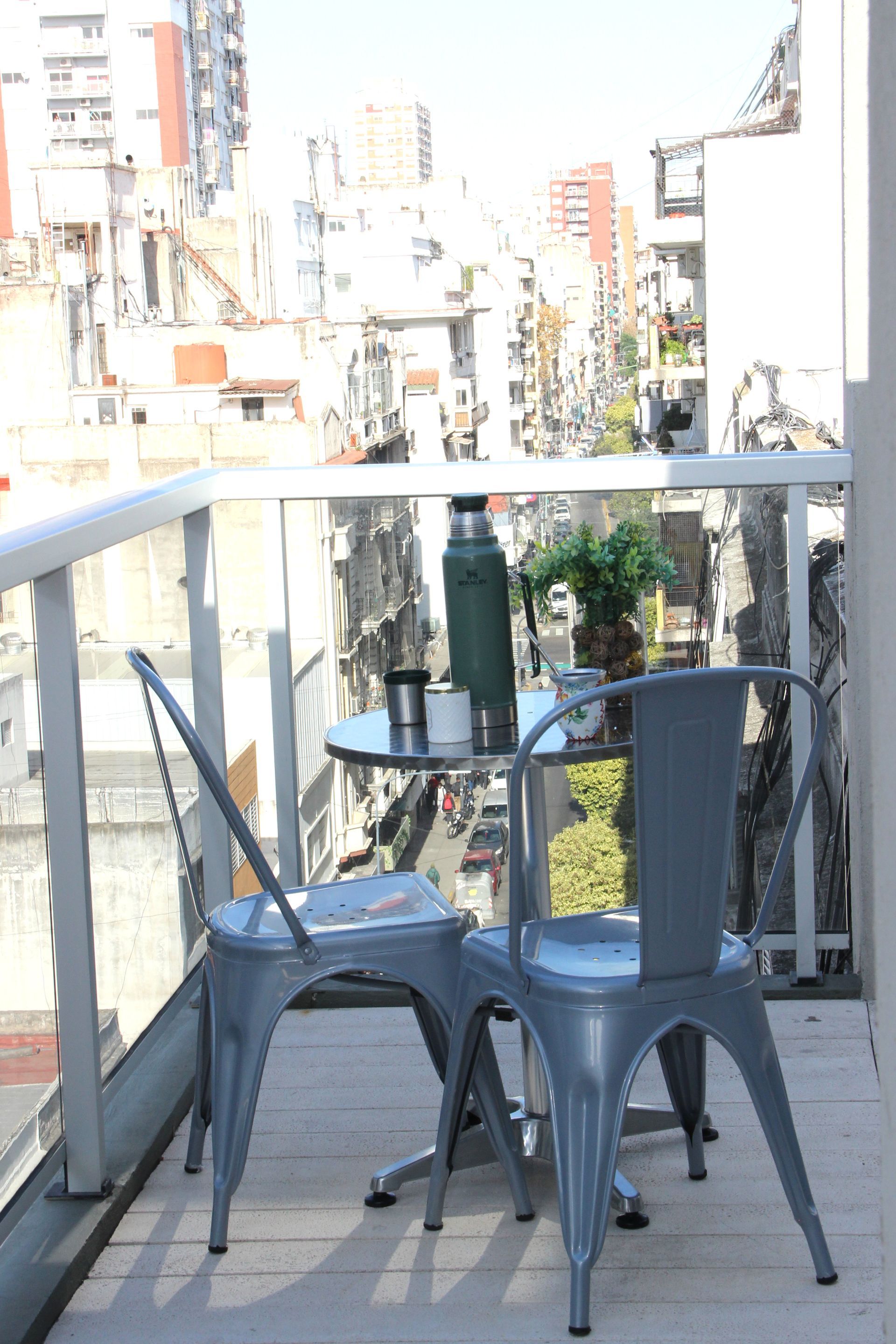 Small balcony with two metal chairs and a round table overlooking a city street