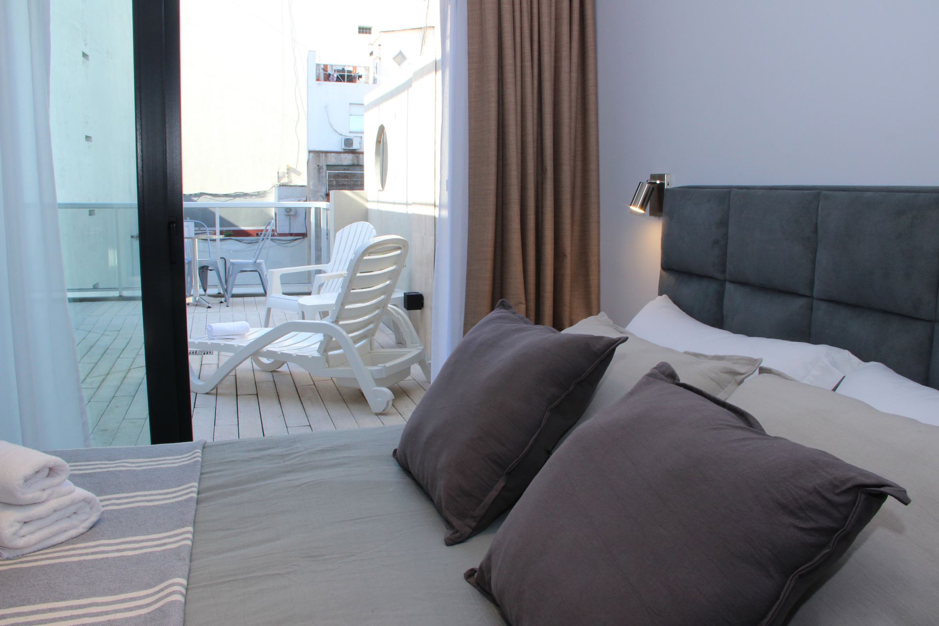 Modern bedroom with gray bed, dark pillows, and balcony view with white patio chairs