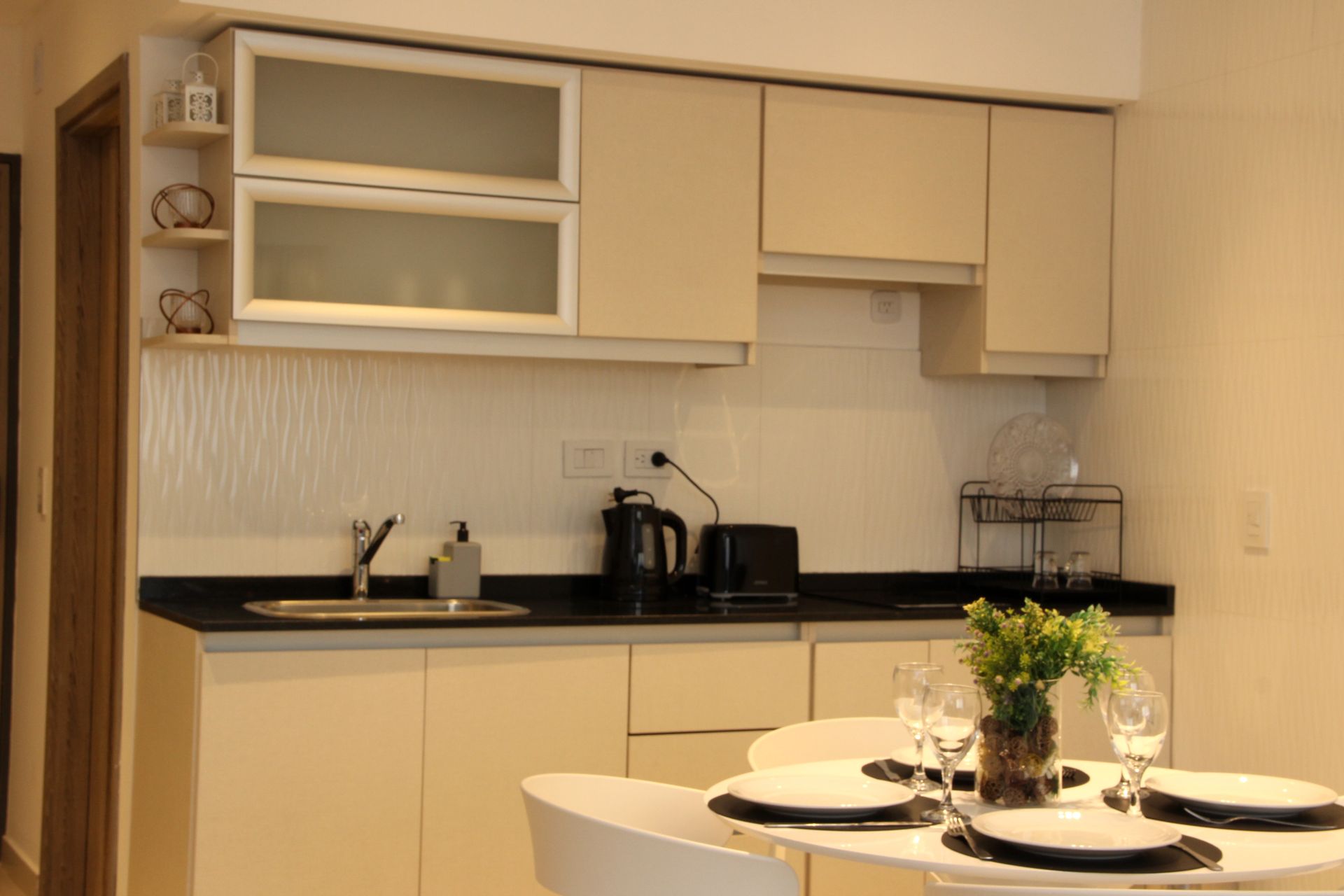 Modern kitchen with beige cabinets, black countertop, and a dining table set with plates and flowers