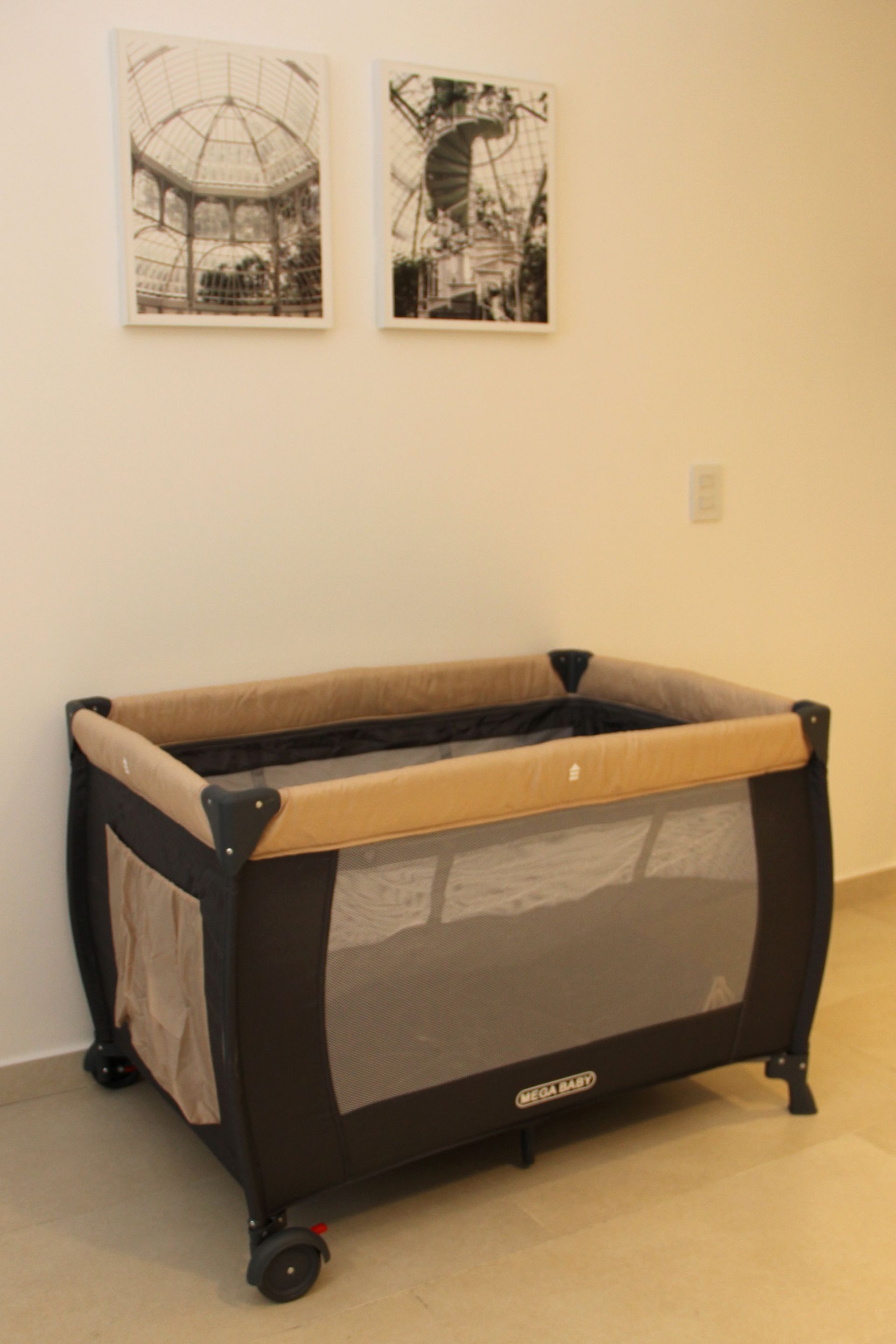 Brown baby crib in a sparse room with two framed pictures on the wall.