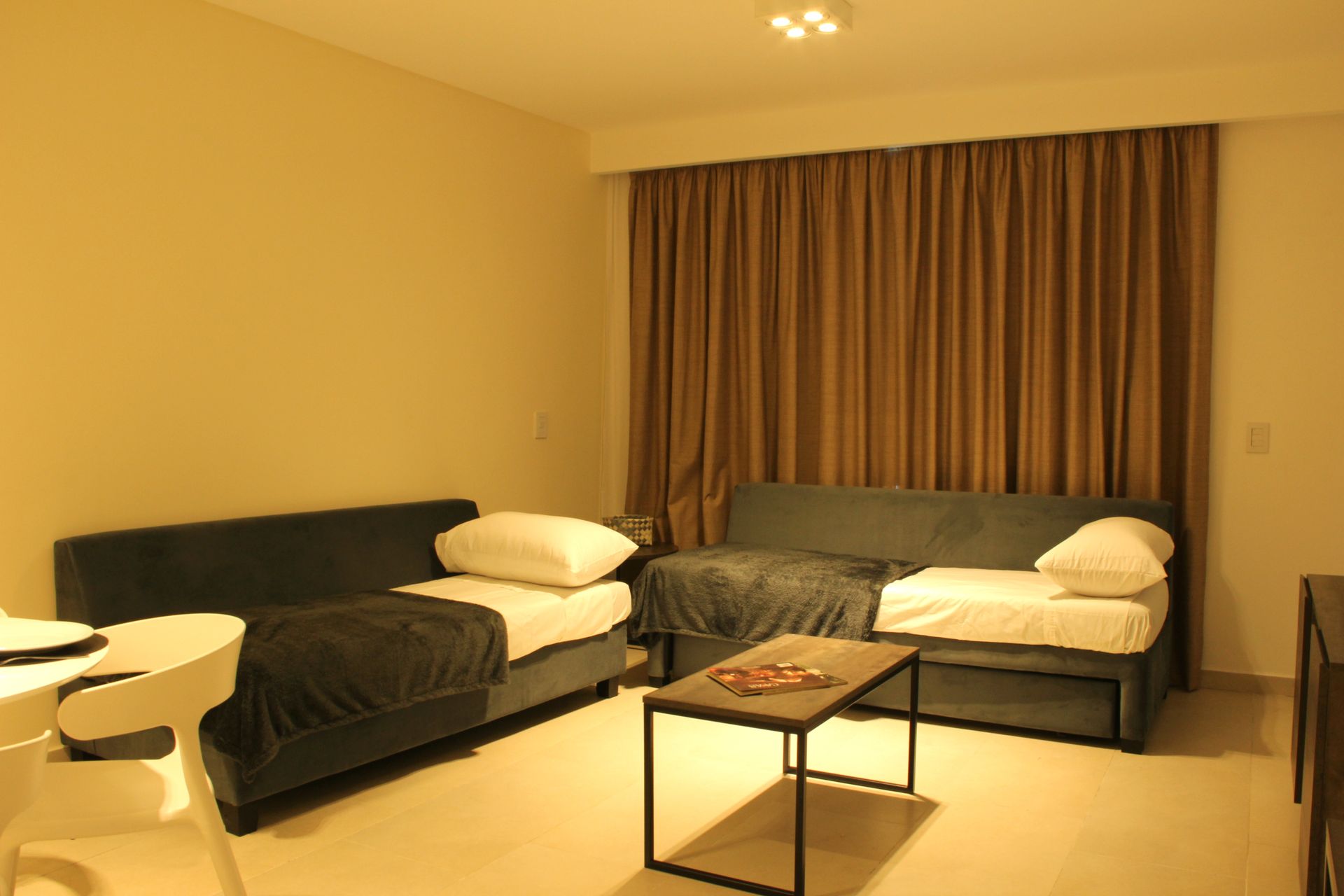 Hotel room with two single beds, a small table, and closed curtains in warm lighting