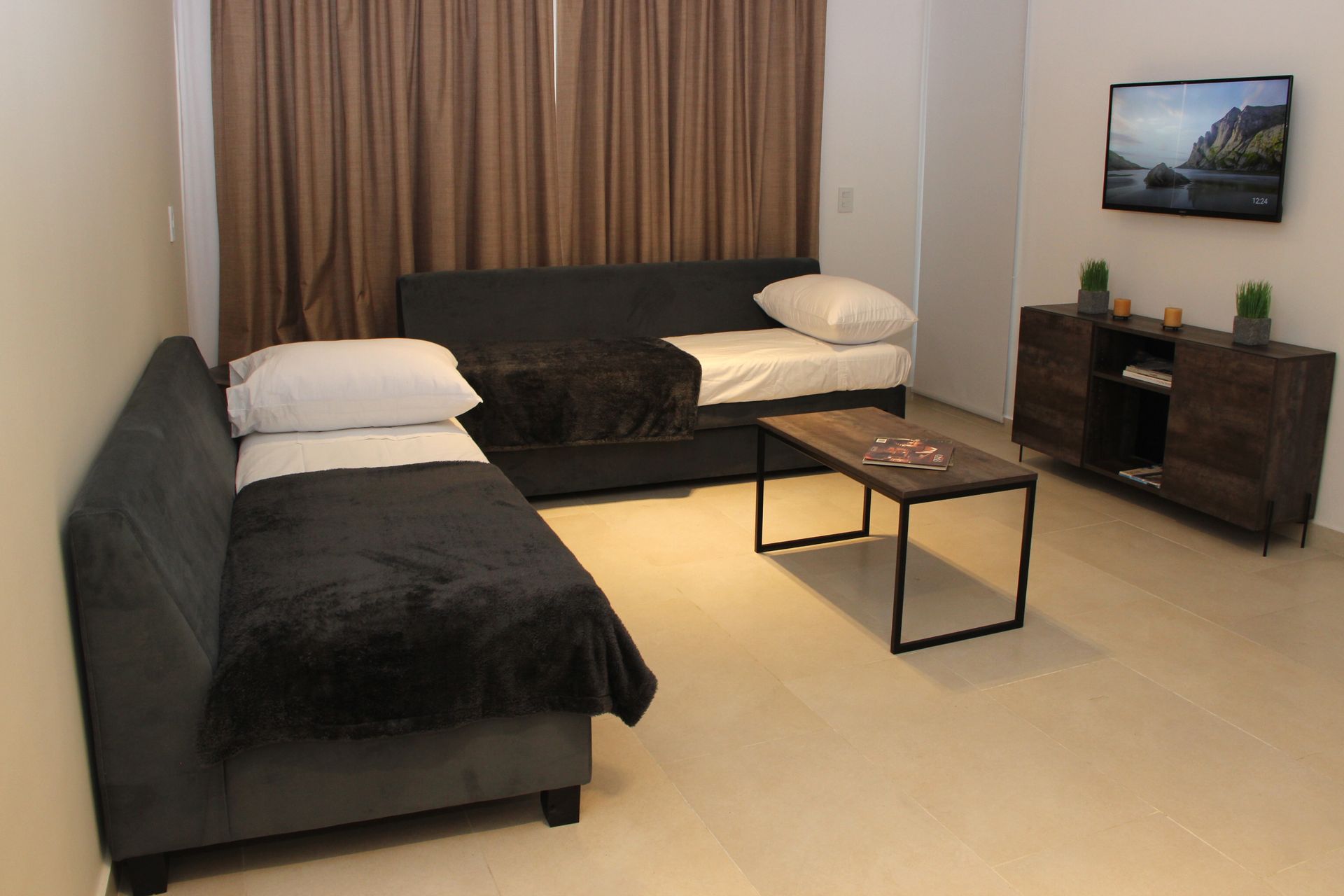 Modern living room with two black sofas, coffee table, TV, and sideboard in a beige room