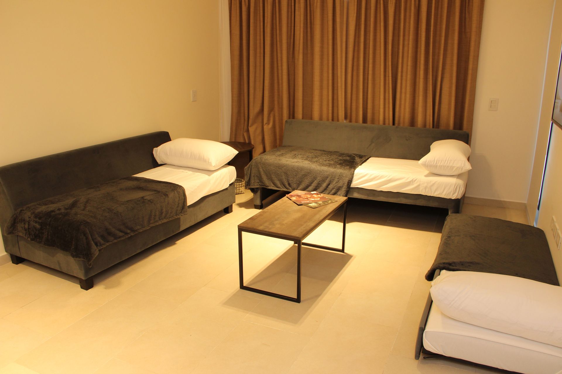 Modern living room with three sofas, coffee table, and brown curtains on beige floor