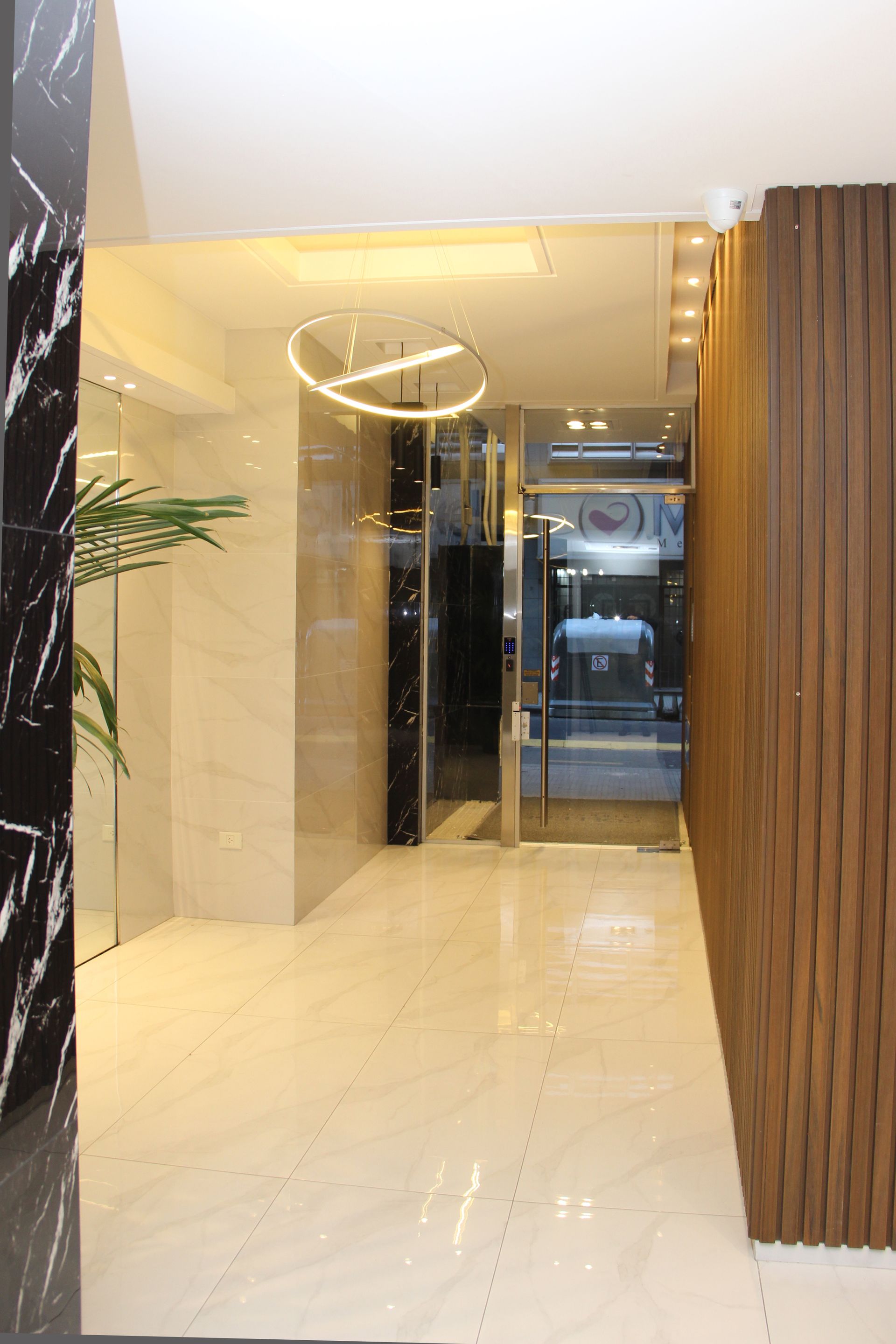 Modern lobby hallway with glossy marble floor, glass doors, and wood-paneled wall accents