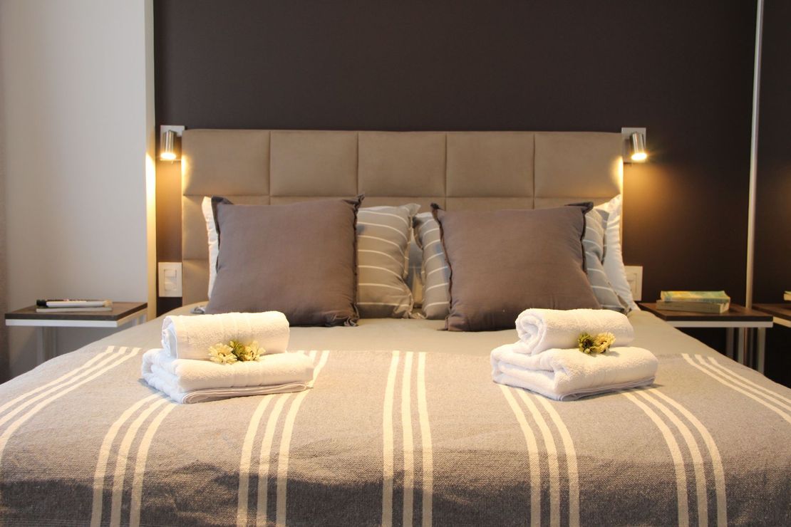 Neatly made hotel bed with gray bedding, two folded towels, and bedside lamps in a modern bedroom.