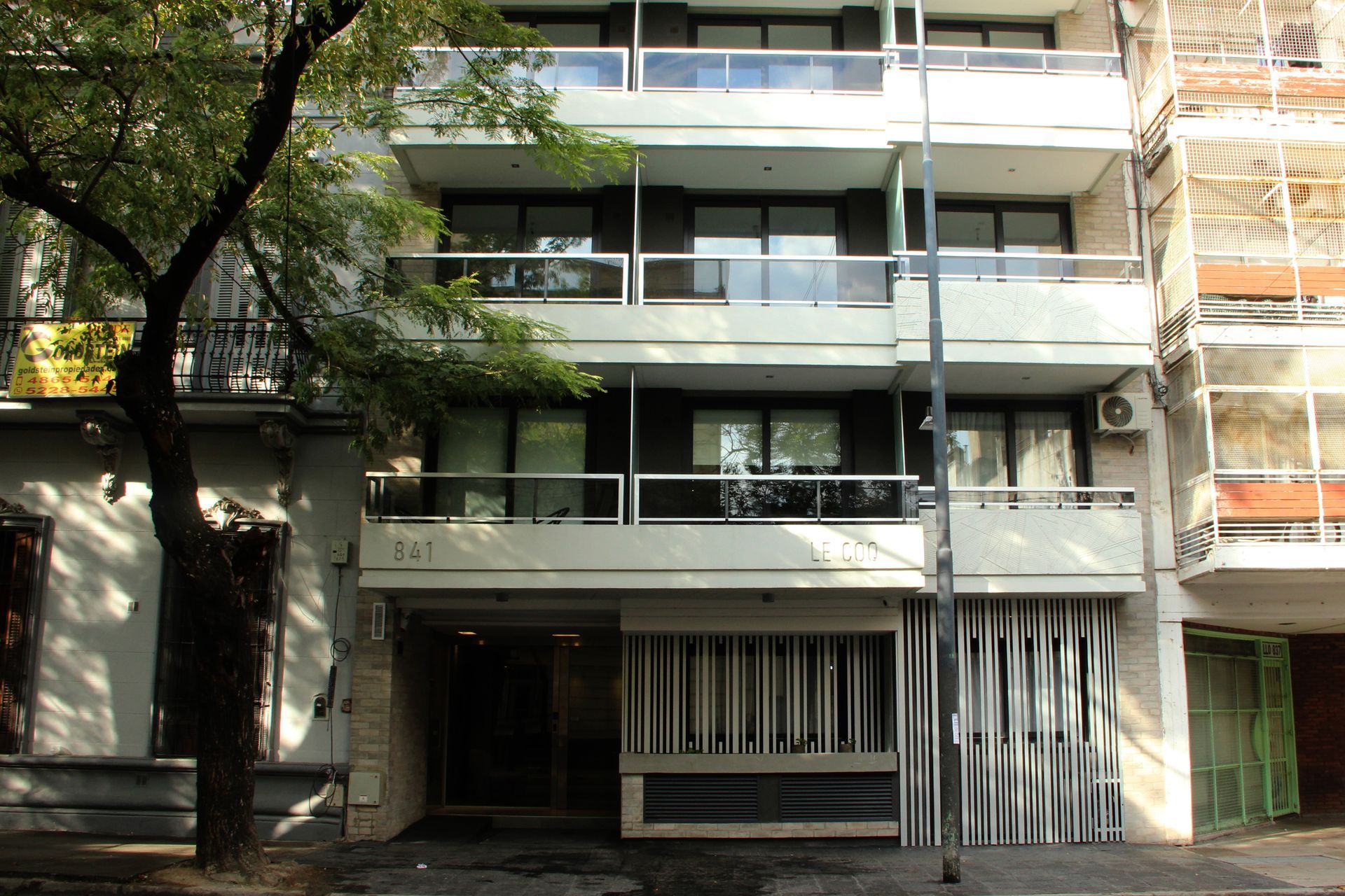 Modern apartment building with balconies, glass railings, and street trees in front
