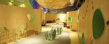 Curved hallway with tan walls, green circular windows, and a sandy floor with tall plant-like sculptures