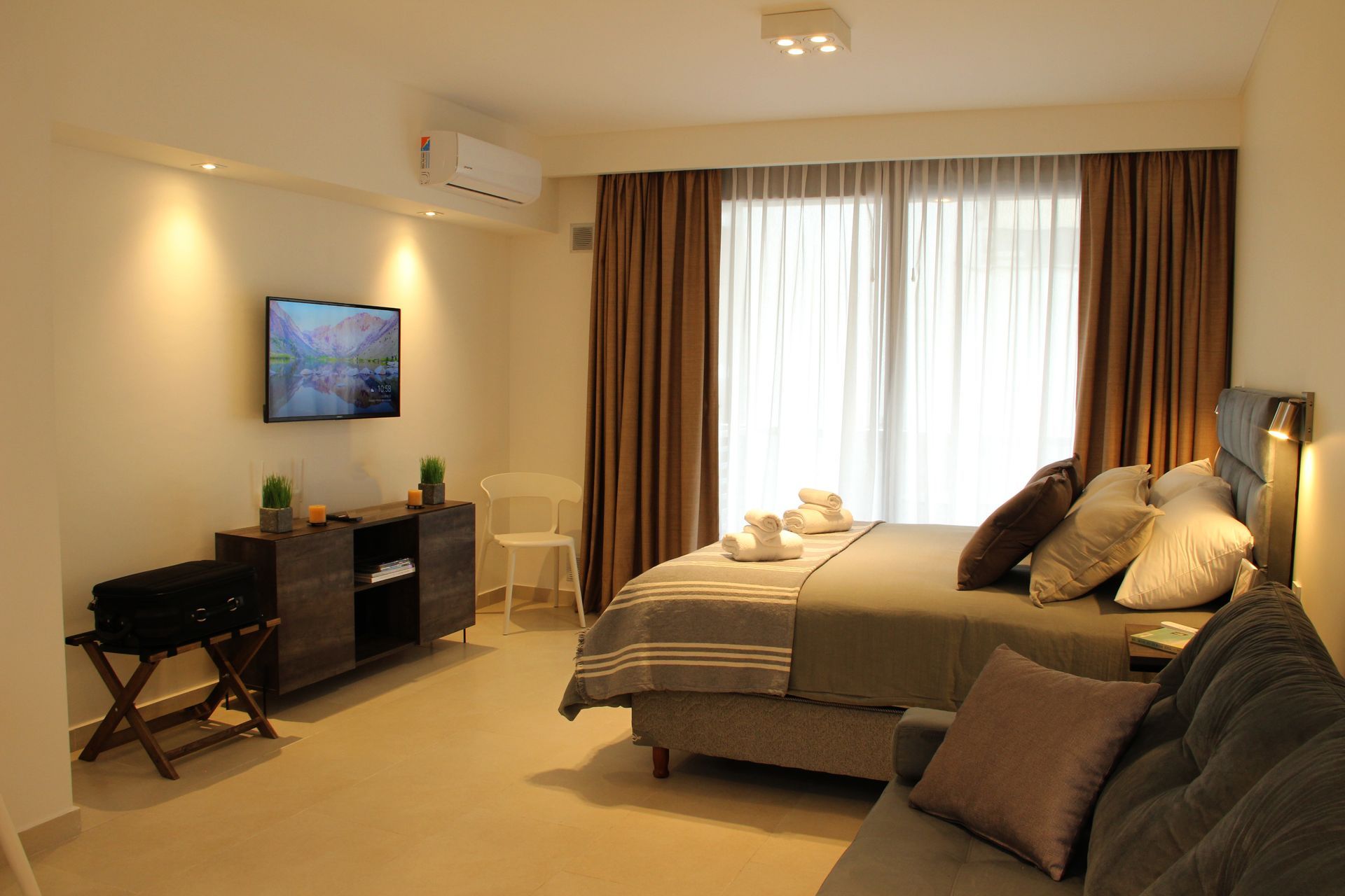 Modern bedroom with bed, sofa, TV, and large window curtains