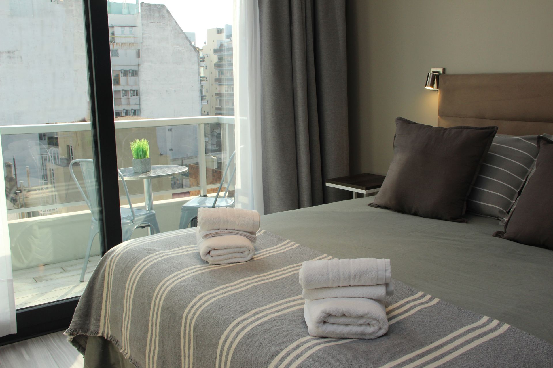 Modern bedroom with a large bed, folded towels, and a balcony view through sliding glass doors