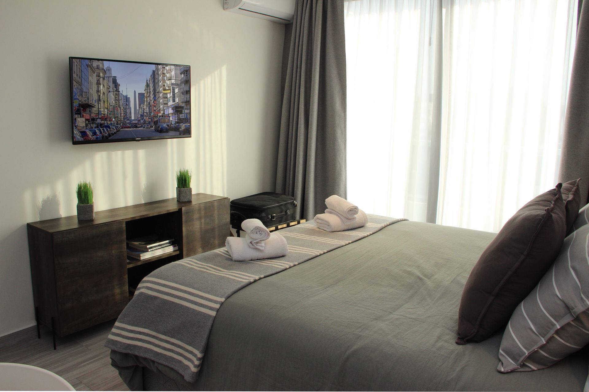 Modern bedroom with gray bedspread, bedside table, wall art, and bright window curtains
