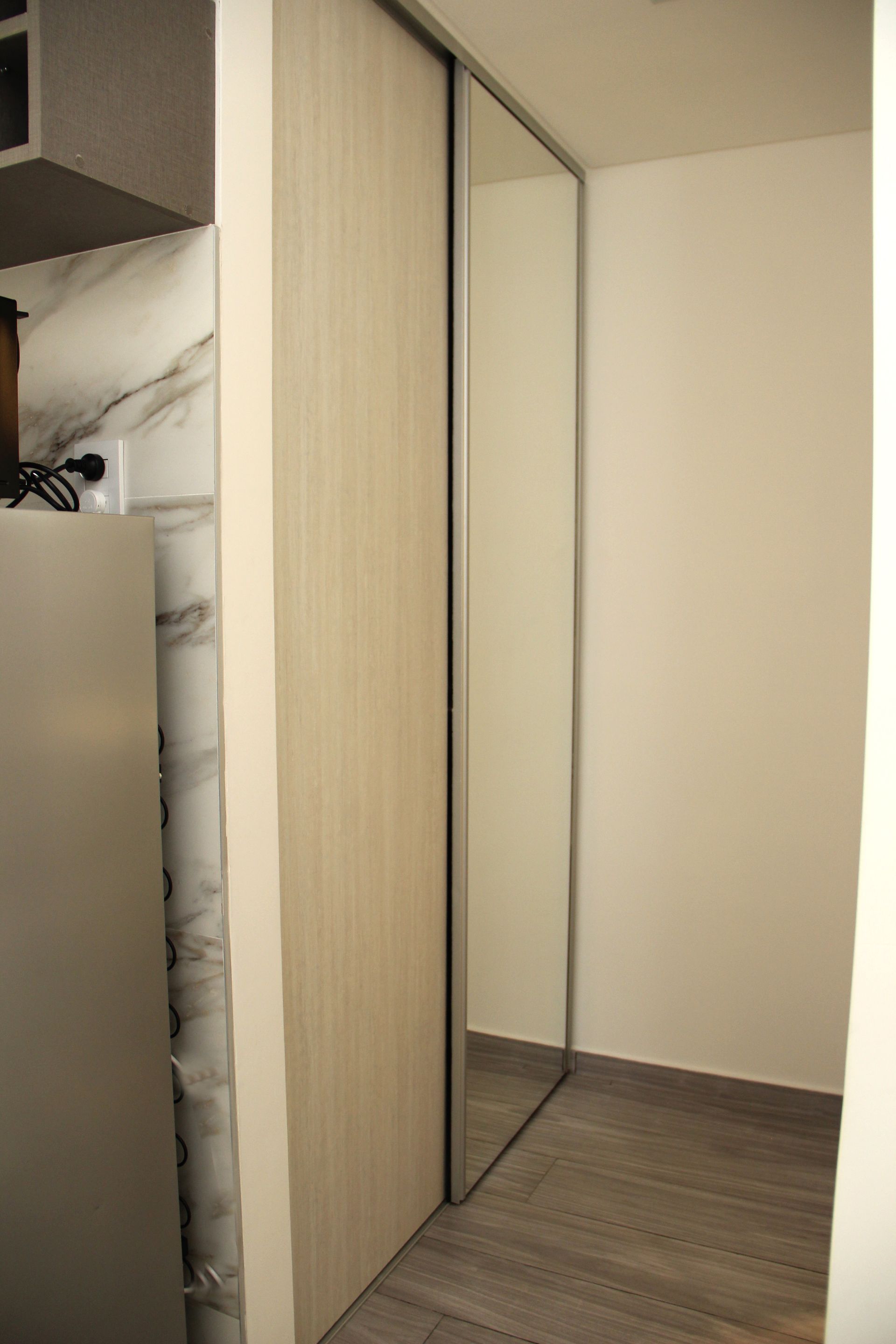 Mirrored closet doors beside a beige wardrobe in a small room with wood flooring