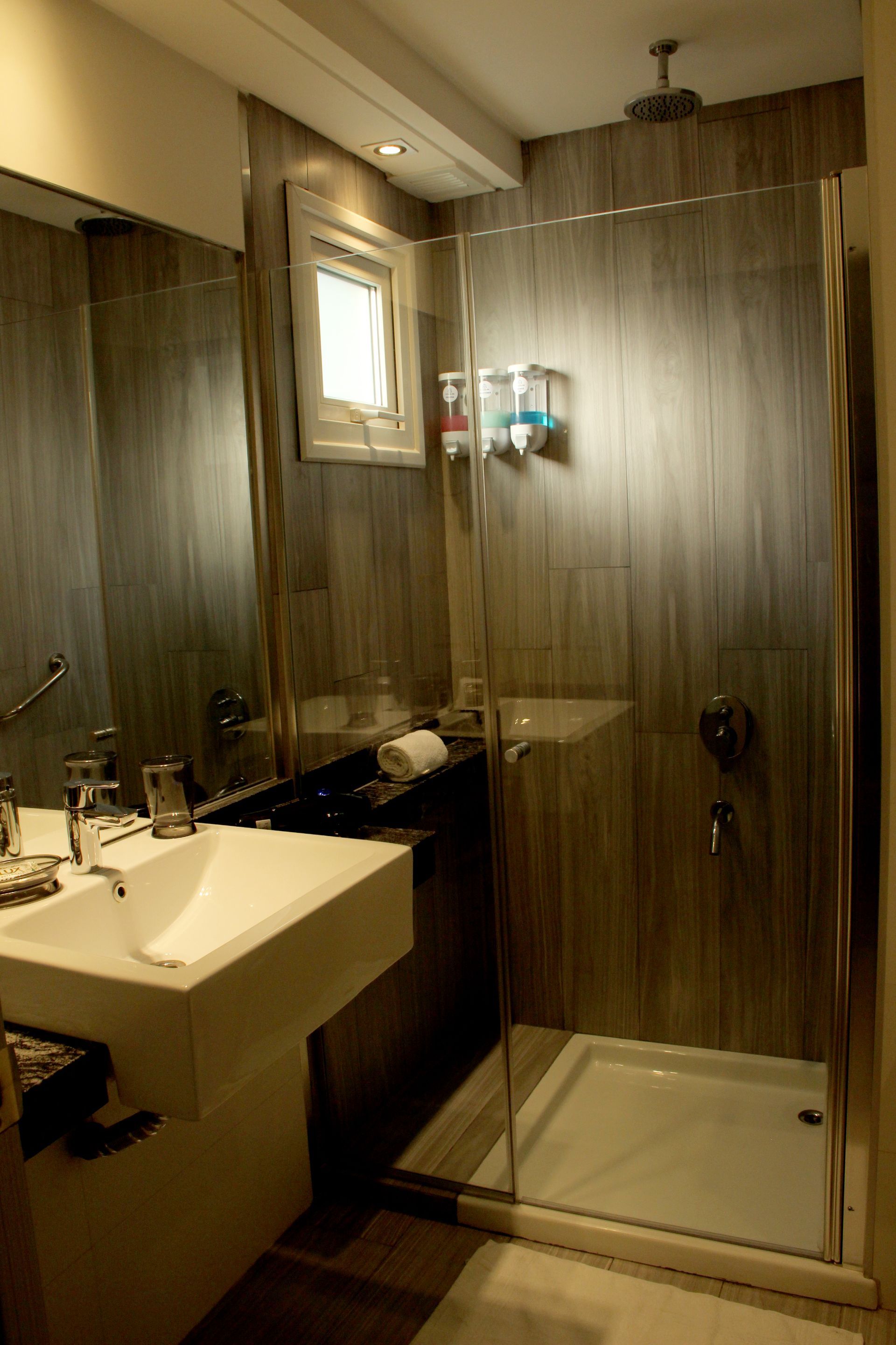 Small modern bathroom with a sink, mirror, window, and glass shower stall.